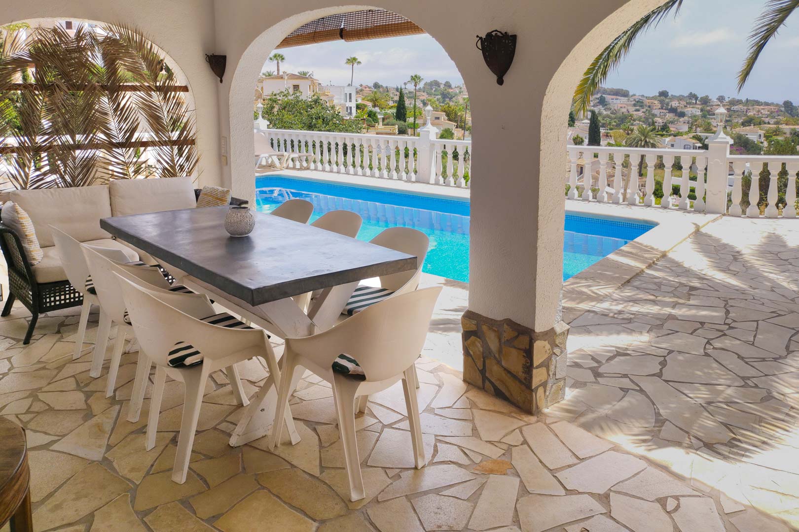 Überdachte Terrasse mit Rundbögen, Natursteinboden und Essbereich mit direktem Blick auf den Pool und das weite Tal mit Palmen.