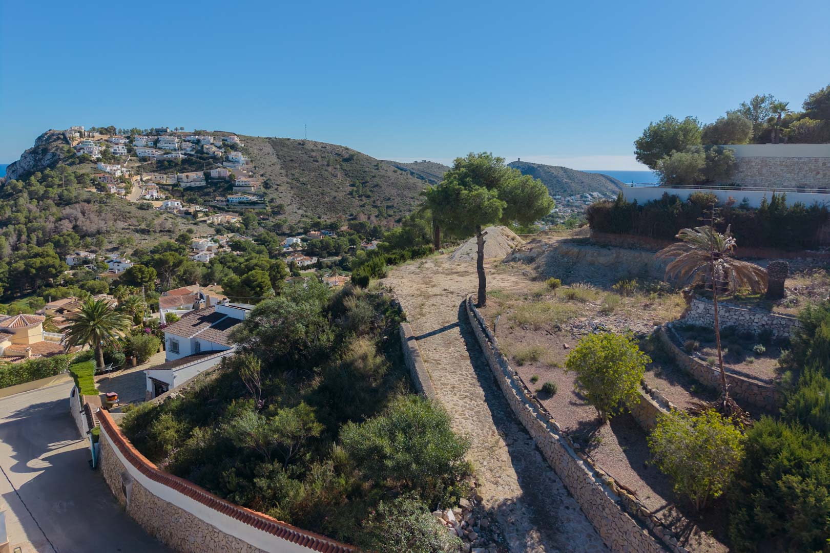 Erhöhte Ansicht des Grundstücks mit Natursteinmauern und mediterraner Vegetation, mit Panoramablick auf das Tal und das Meer in Moraira.