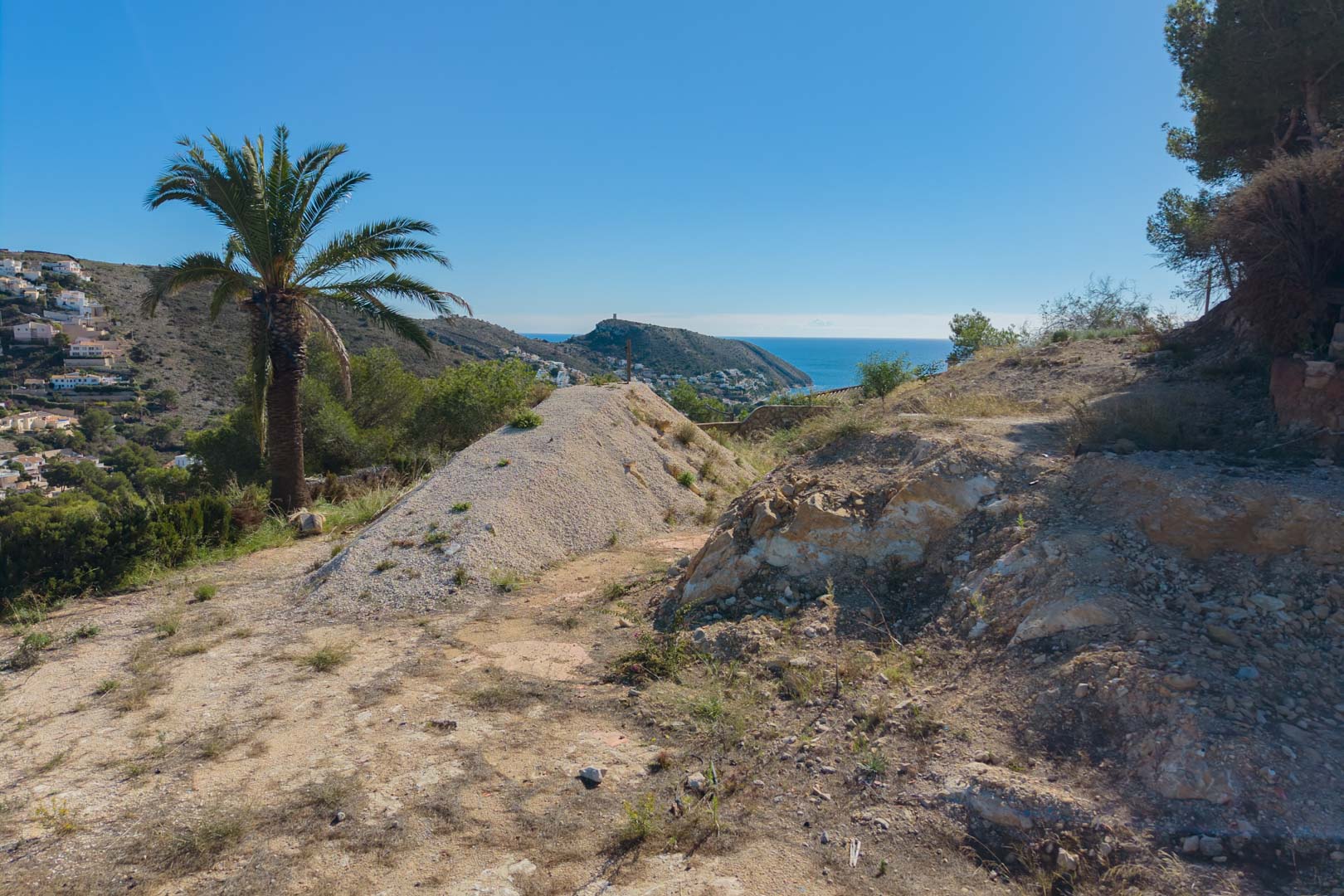 Erhöhtes Baugrundstück in der Vorbereitungsphase mit Panoramablick auf das Mittelmeer und die Küste von Moraira, umgeben von mediterraner Flora.
