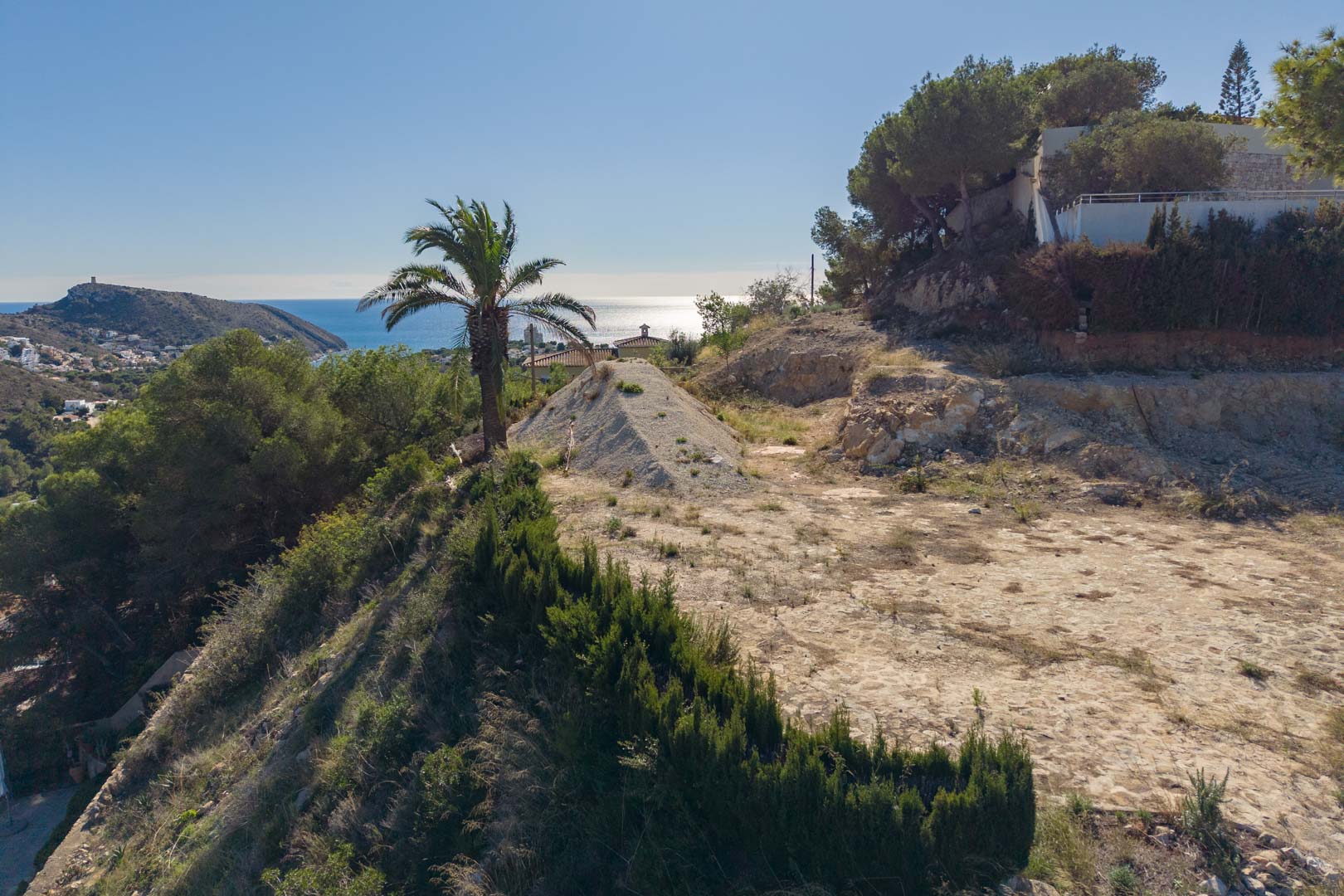 Erhöhtes Baugrundstück in Moraira mit Panoramablick auf das Mittelmeer und El Portet, eingebettet in eine natürliche Umgebung mit Pinienbestand.