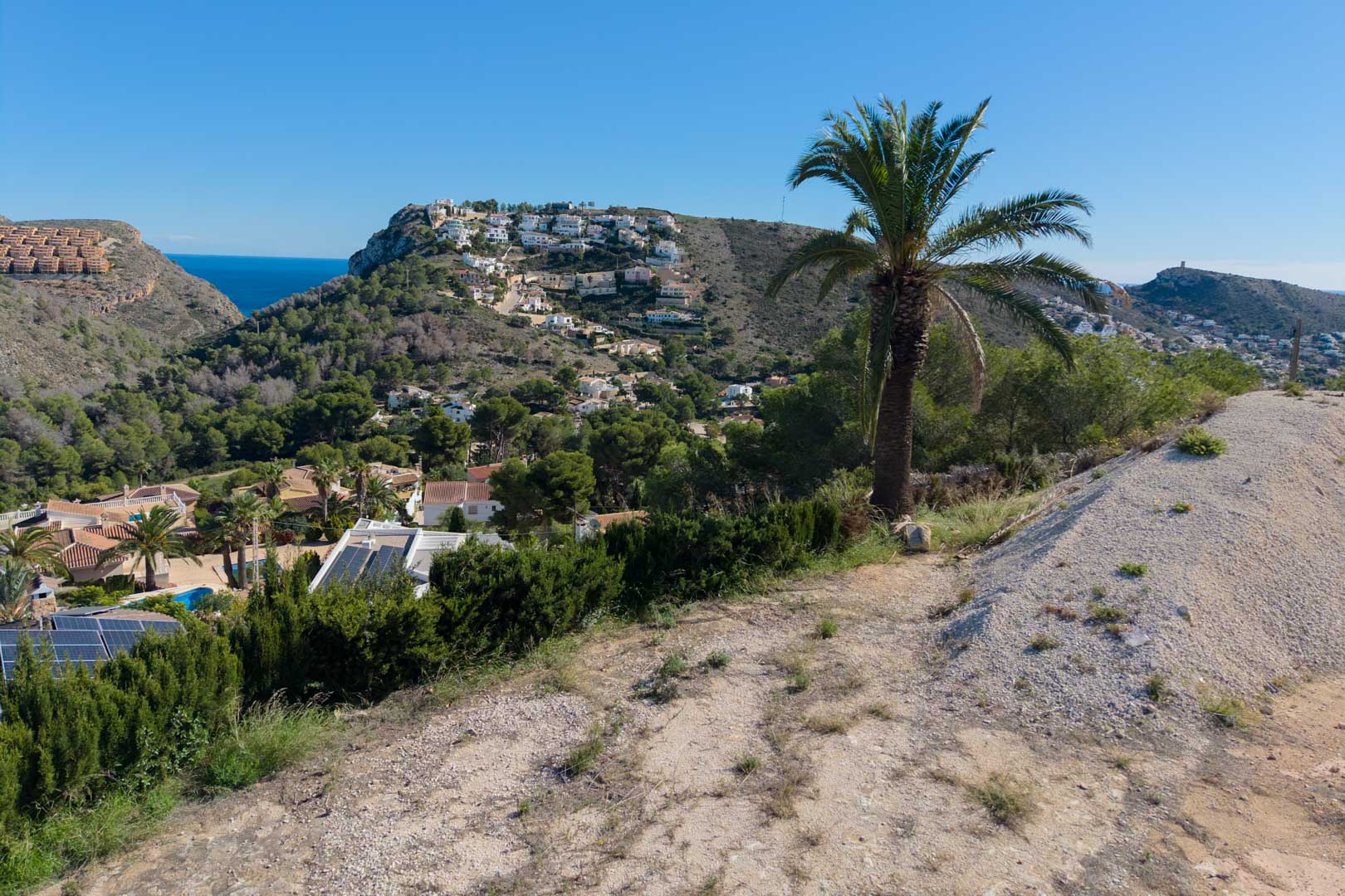 Panoramablick vom erhöhten Grundstück über das Tal von Moraira, mit dem Mittelmeer im Hintergrund und bewaldeten Hügeln mit Pinien und Palmen.