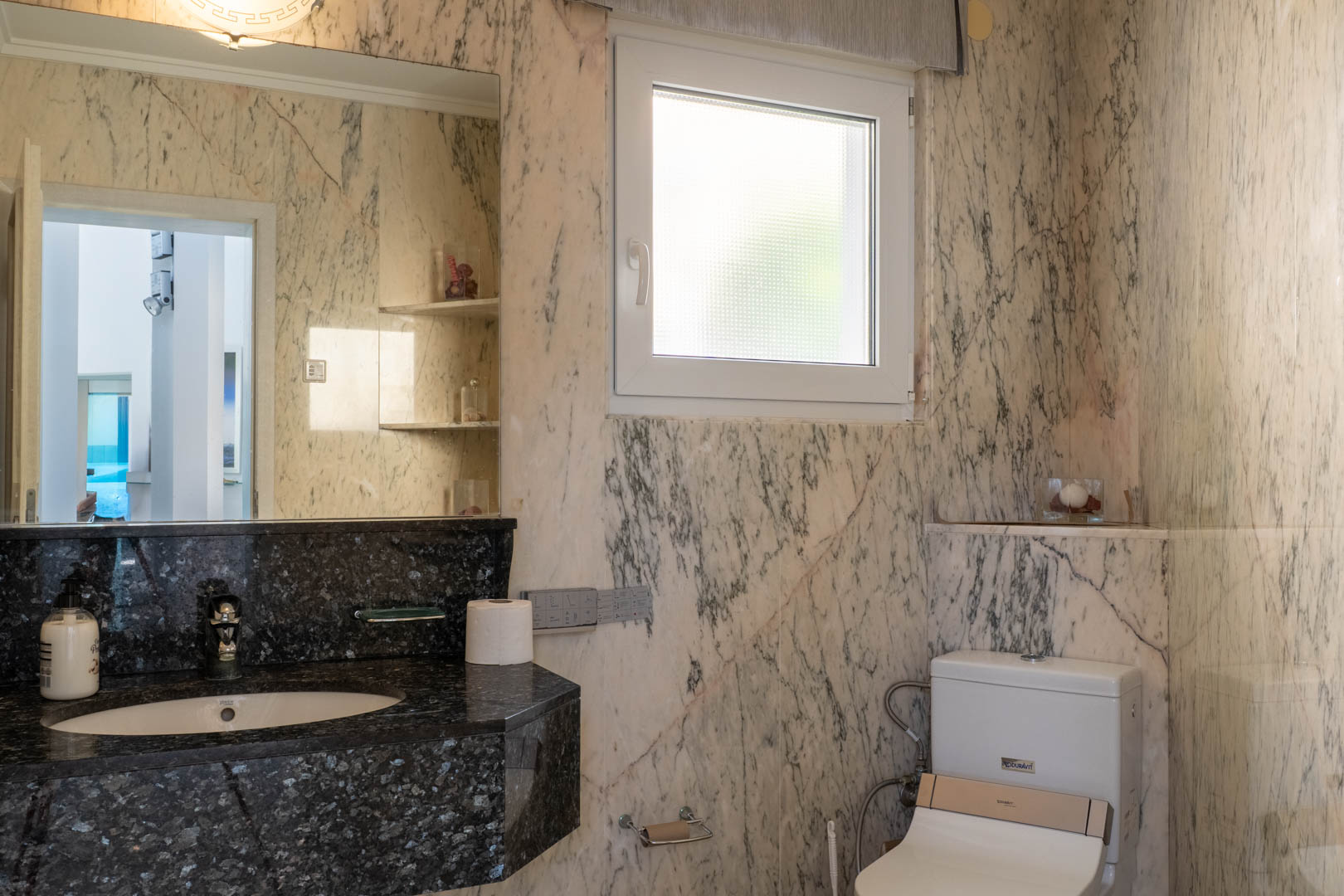 Badezimmer mit marmorierten Wänden und schwarzer Granitplatte.