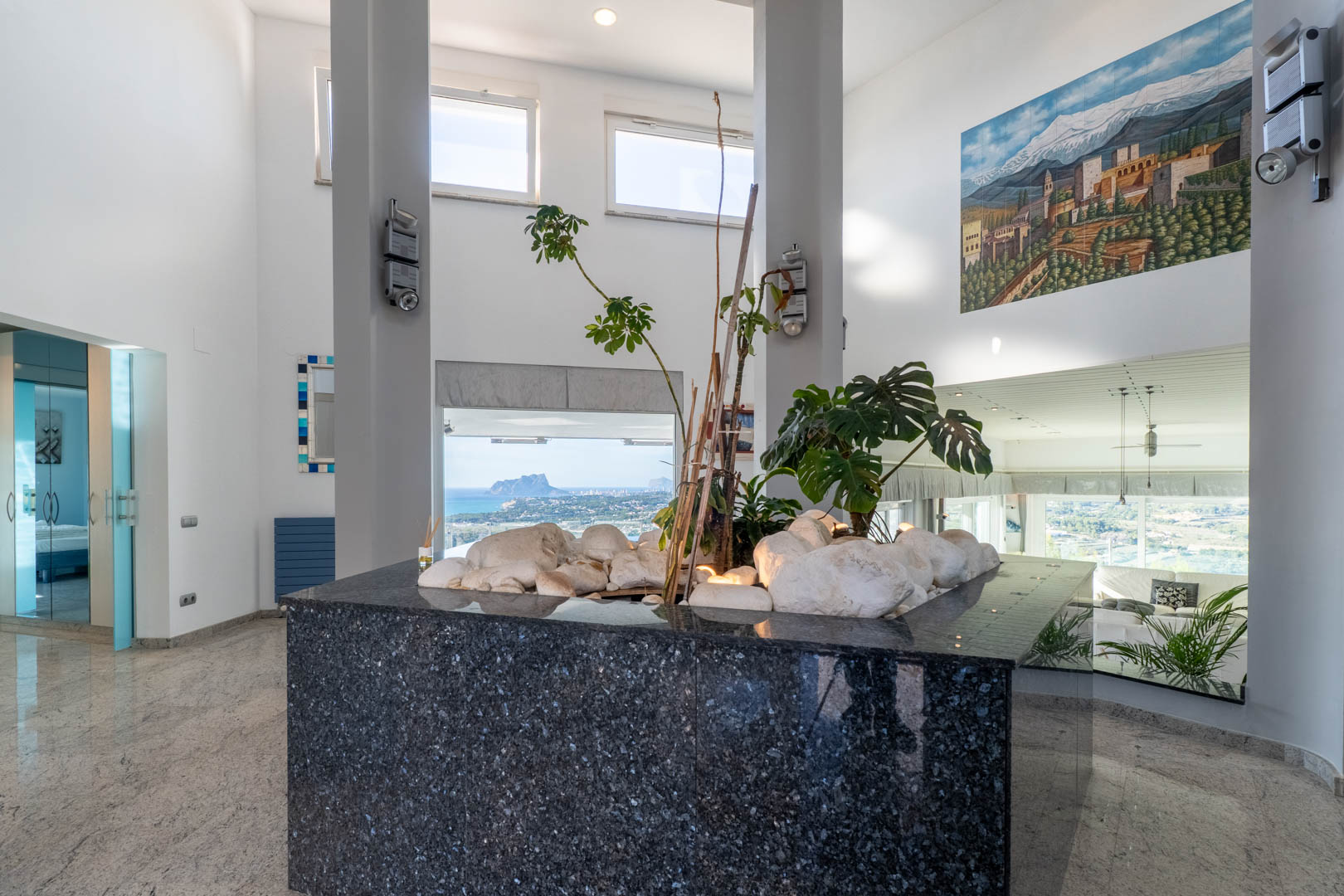 Innendetail mit polierter Granitplatte, Pflanzen und Küstenblick durch große Fenster.