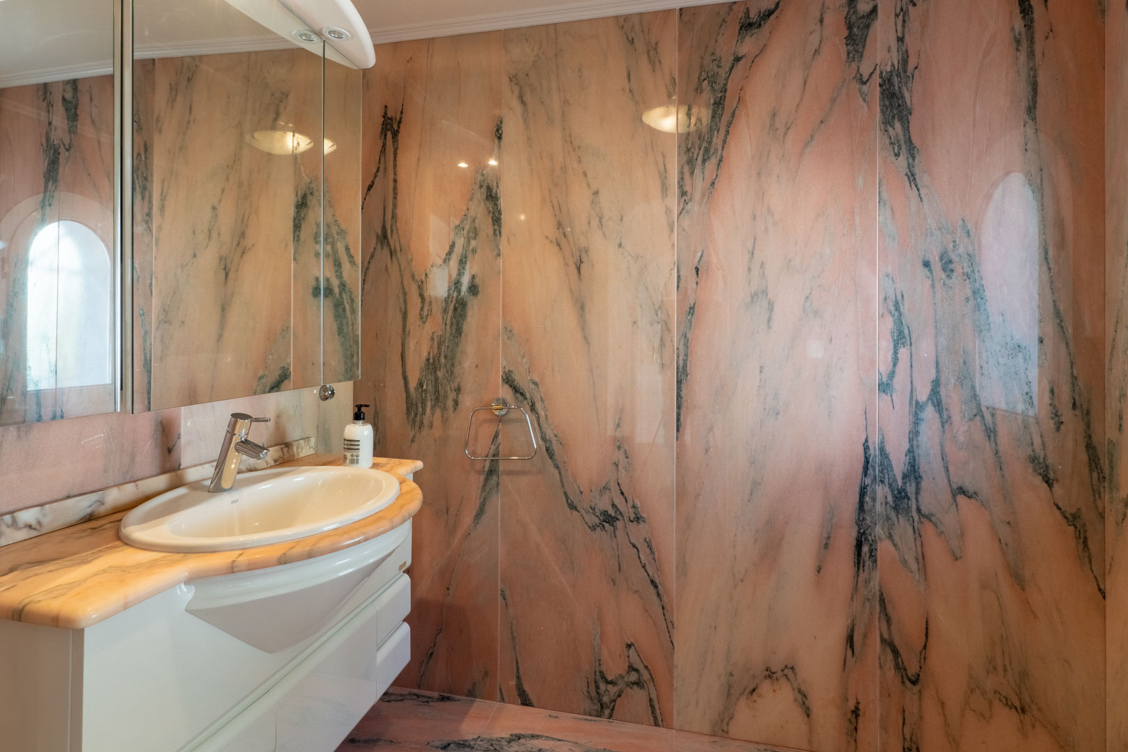 Badezimmer mit vollflächiger Wandverkleidung aus rosa Marmor mit dunkler Maserung. Ausgestattet mit passender Steinplatte, weißem Waschtisch und großem Spiegel.