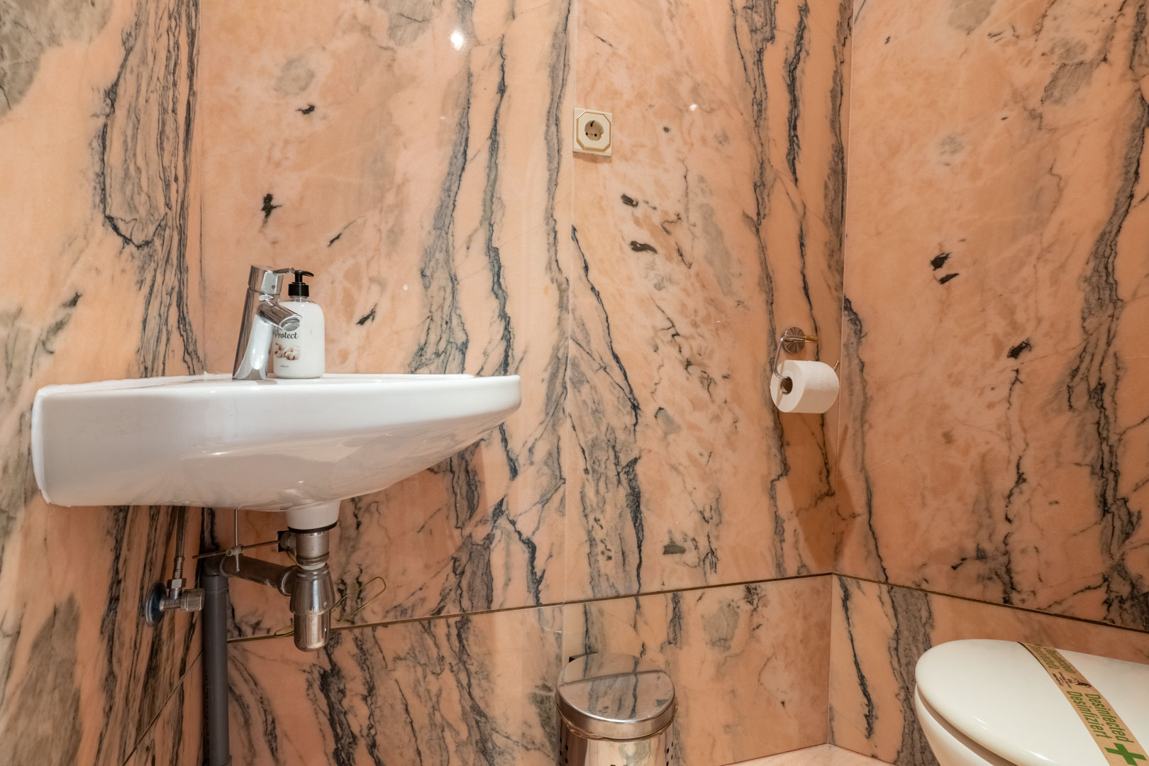Gäste-WC mit einer Wandverkleidung aus rosa Marmor mit dunkler Maserung, ausgestattet mit einem weißen Hängewaschbecken.