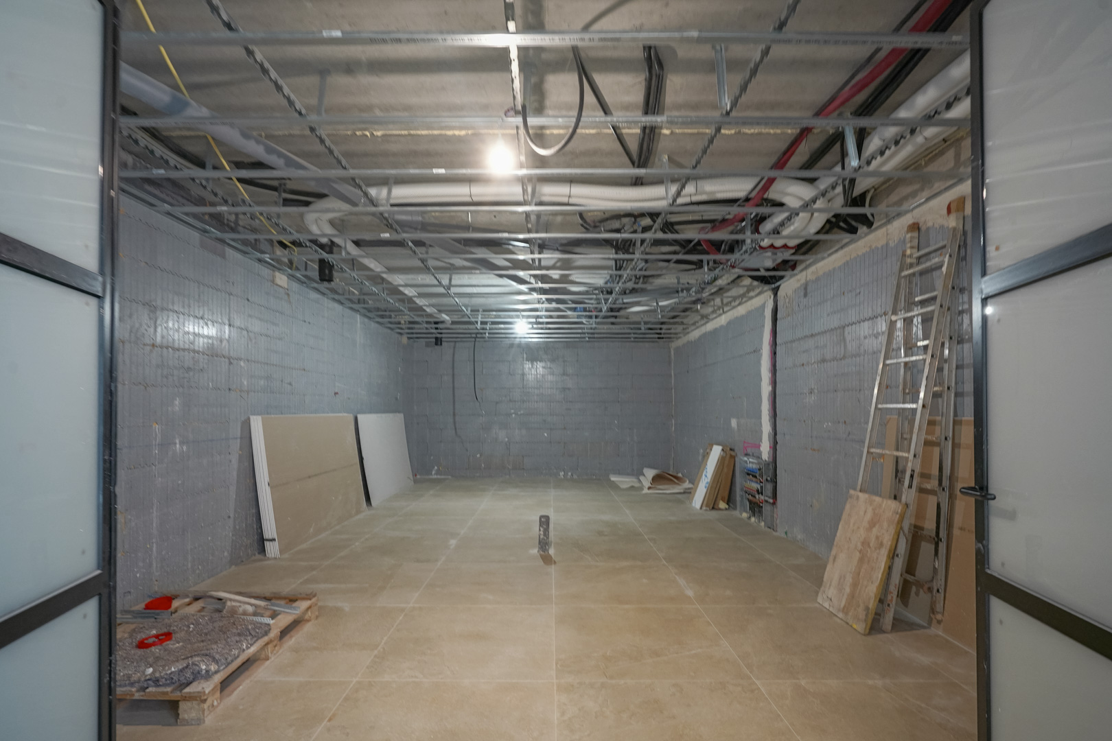 Großzügiges, 180 m2 großes Untergeschoss im Rohbau mit Styro-Stone-Wänden, sichtbarer Deckeninstallation und Schiebetüren mit schwarzem Rahmen.
