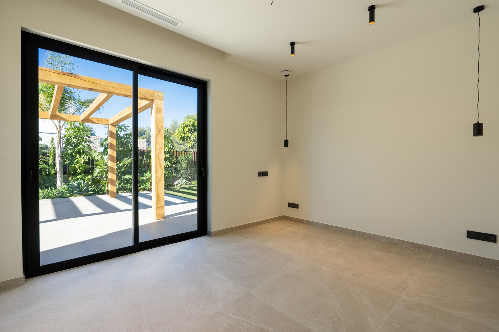 Minimalistisches Interieur mit Keramikboden und großen Glasschiebetüren zur Außenterrasse mit Holzpergola und mediterraner Bepflanzung.