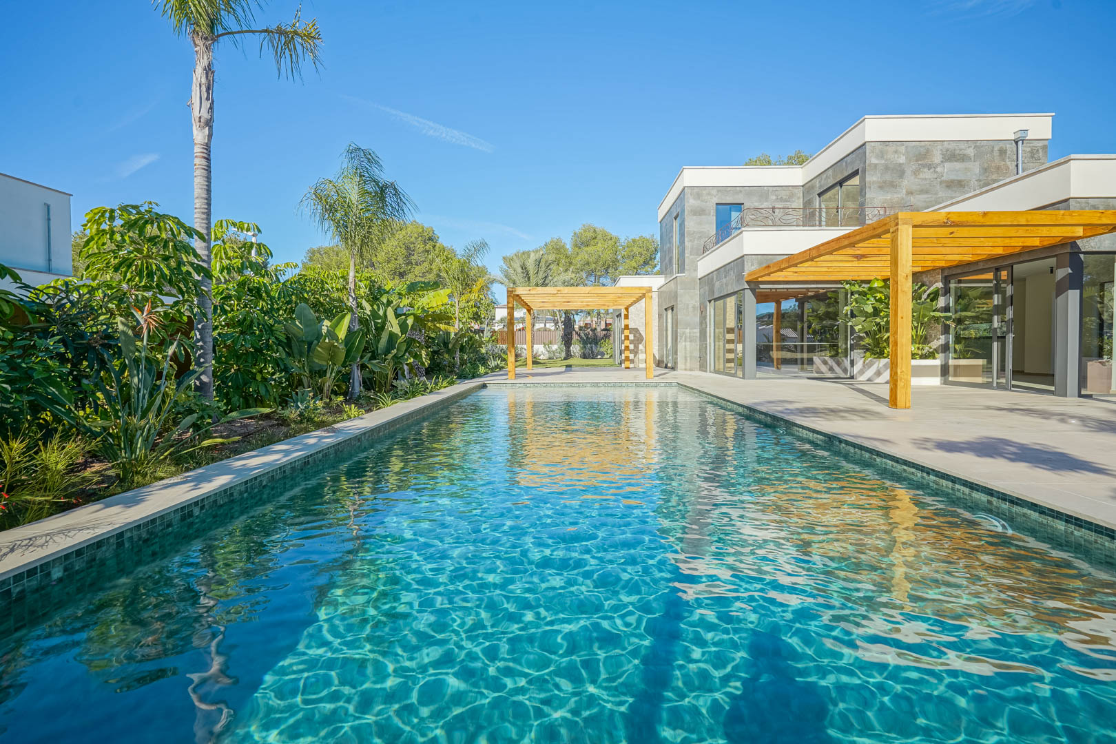 Pool im Bali-Stil mit smaragdgrünen Fliesen, umgeben von einer Terrasse mit Iroko-Holzpergolen und einem üppigen mediterranen Garten.