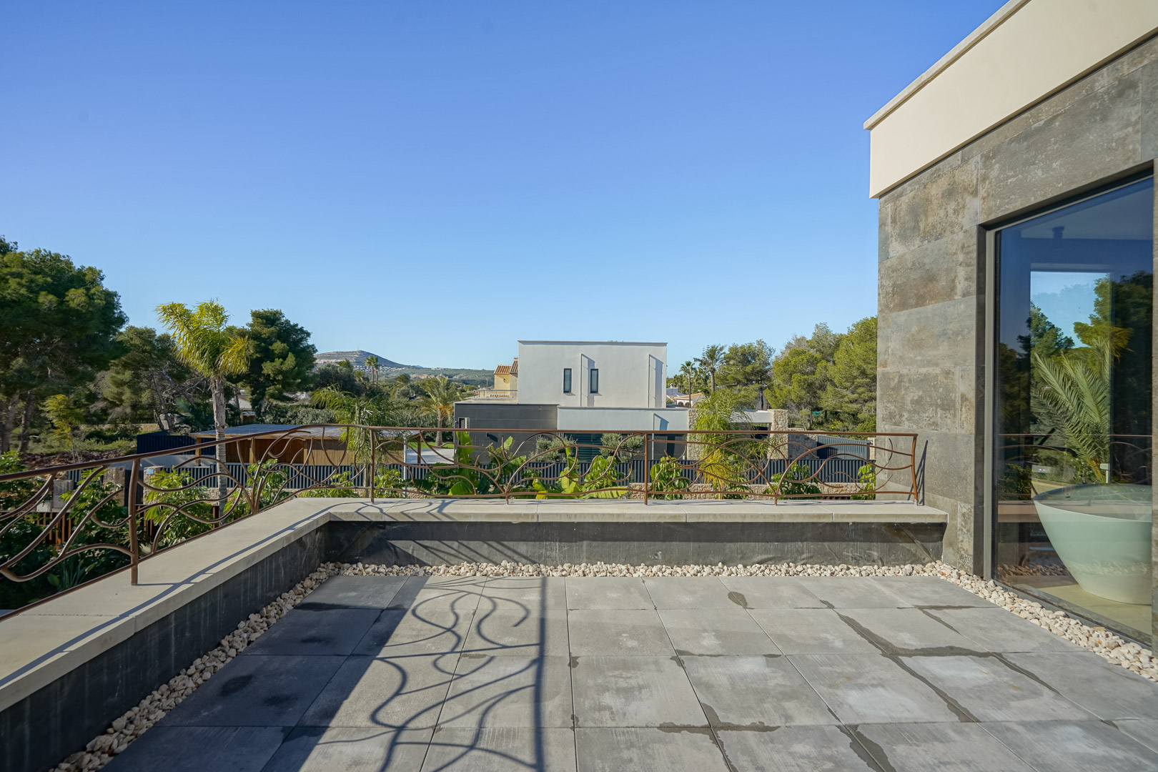 Private Dachterrasse im Obergeschoss mit grauen Steinplatten, kunstvollem Eisengeländer und weitem Blick über die mediterrane Umgebung.