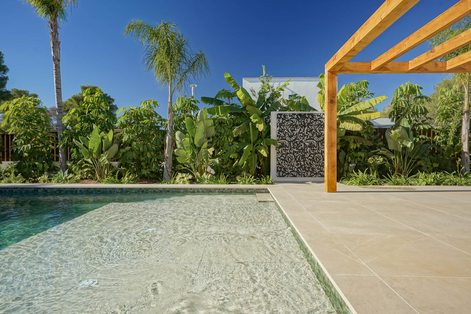 Salzwasserpool im Bali-Stil mit Flachwasserzone, umgeben von einer großzügigen Terrasse, einer Iroko-Holzpergola und üppiger mediterraner Bepflanzung.