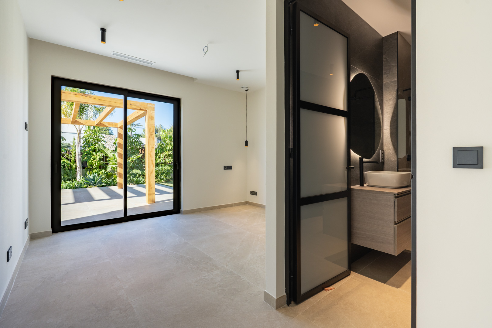 Schlafzimmer mit Terrassenzugang und Holzpergola. Es bietet ein En-Suite-Bad mit Aufsatzwaschbecken, hintergrundbeleuchtetem Spiegel und schwarzen Armaturen.