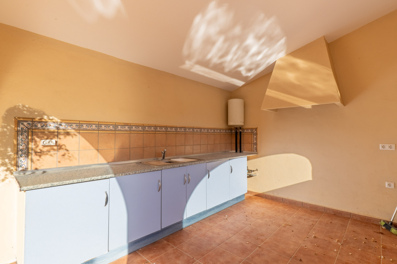 Funktionale Außenküche mit Granitarbeitsplatte, hellblauen Unterschränken und traditionellem Fliesenspiegel. Ausgestattet mit Edelstahlspüle und großer Dunstabzugshaube.
