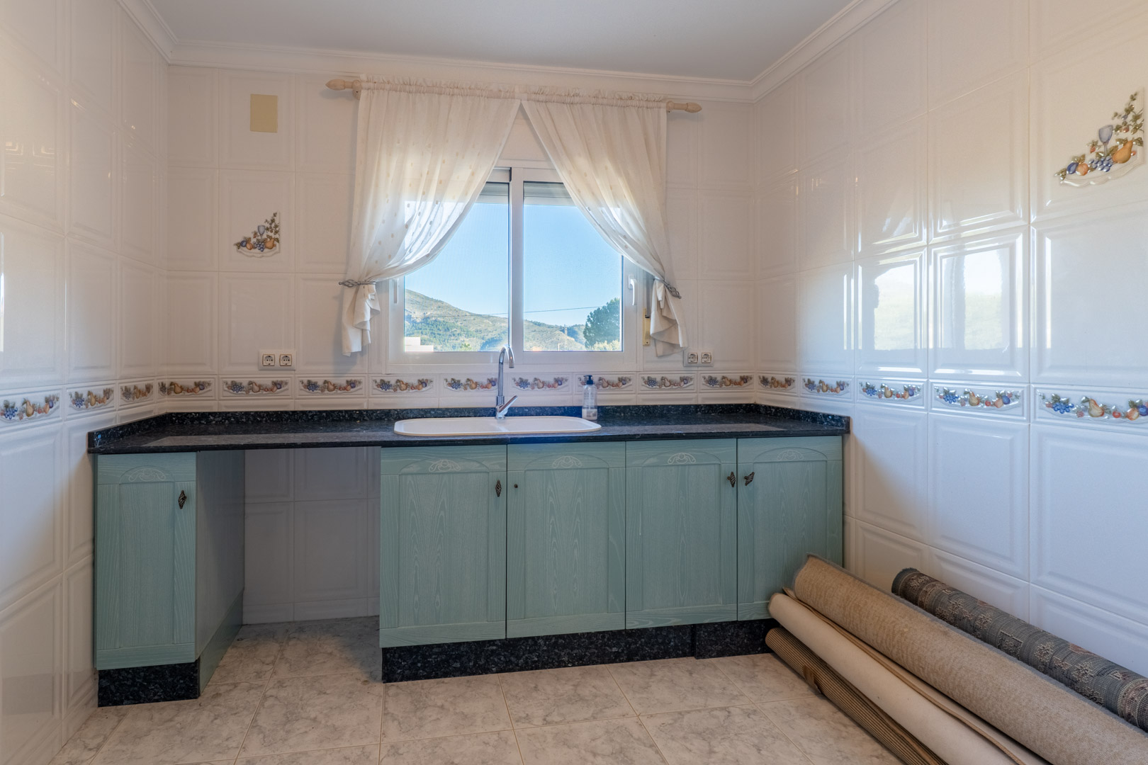Funktionale Küche mit hellblauen Holzschränken, dunkler Granitarbeitsplatte und einem Fenster mit Blick auf die umliegende Berglandschaft.