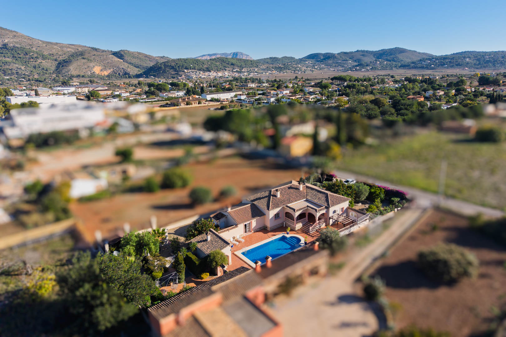 Luftaufnahme der mediterranen Villa in Jalón, die den privaten Pool, die Terrasse und das flache Grundstück inmitten der bergigen Tallandschaft zeigt.