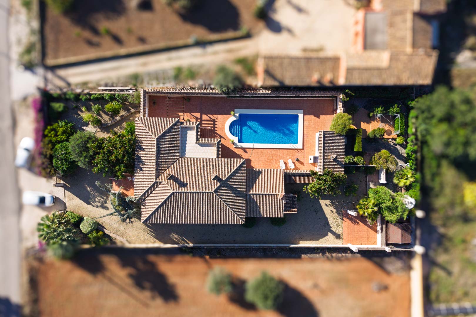 Luftaufnahme der Villa auf einem flachen Grundstück mit rechteckigem Pool, weitläufigen gepflasterten Terrassen und traditionellem Ziegeldach.