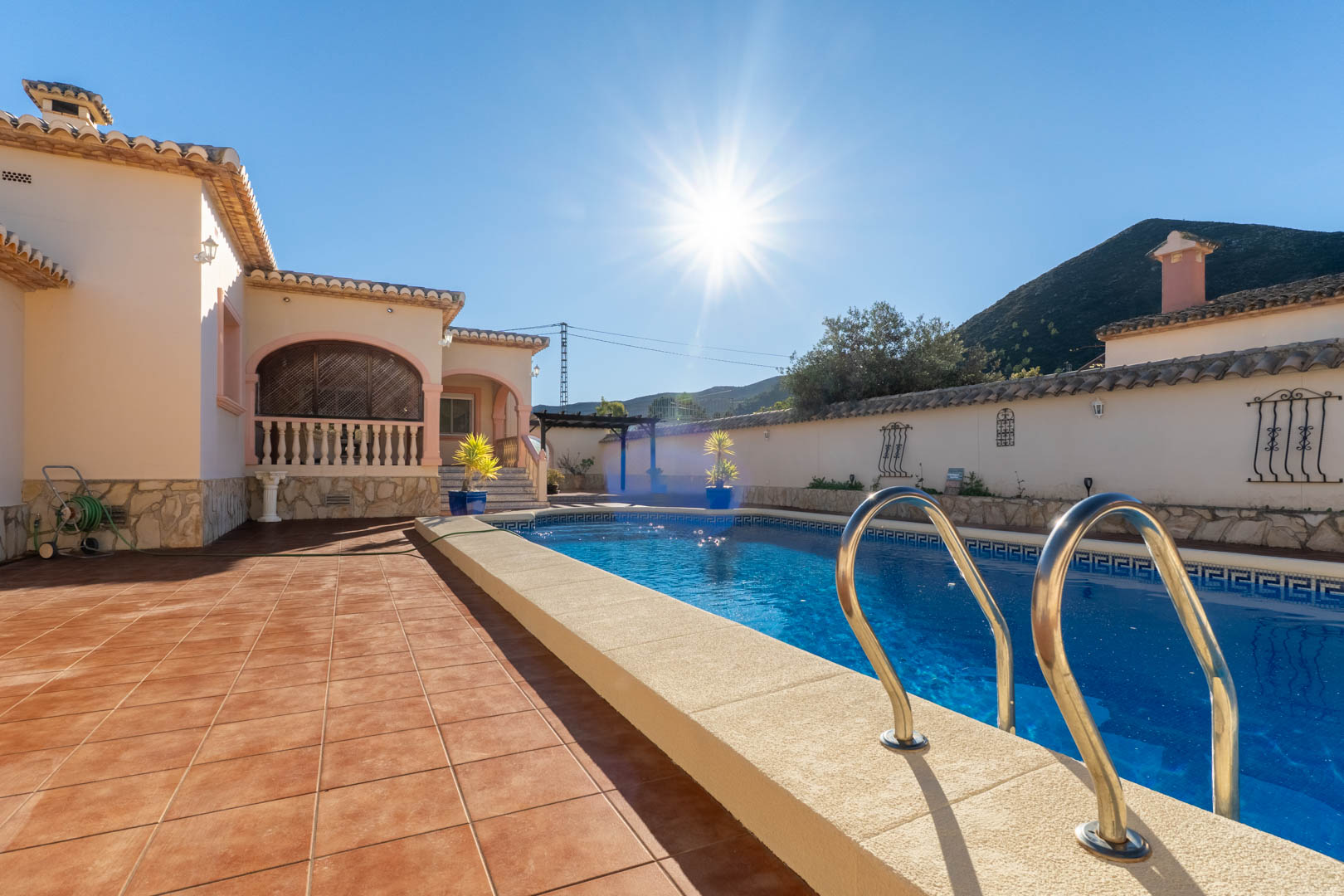 Privater Pool mit griechischem Mosaikrand, umgeben von einer großzügigen Terrasse in Terrakotta-Optik und mit Blick auf die umliegende Berglandschaft.