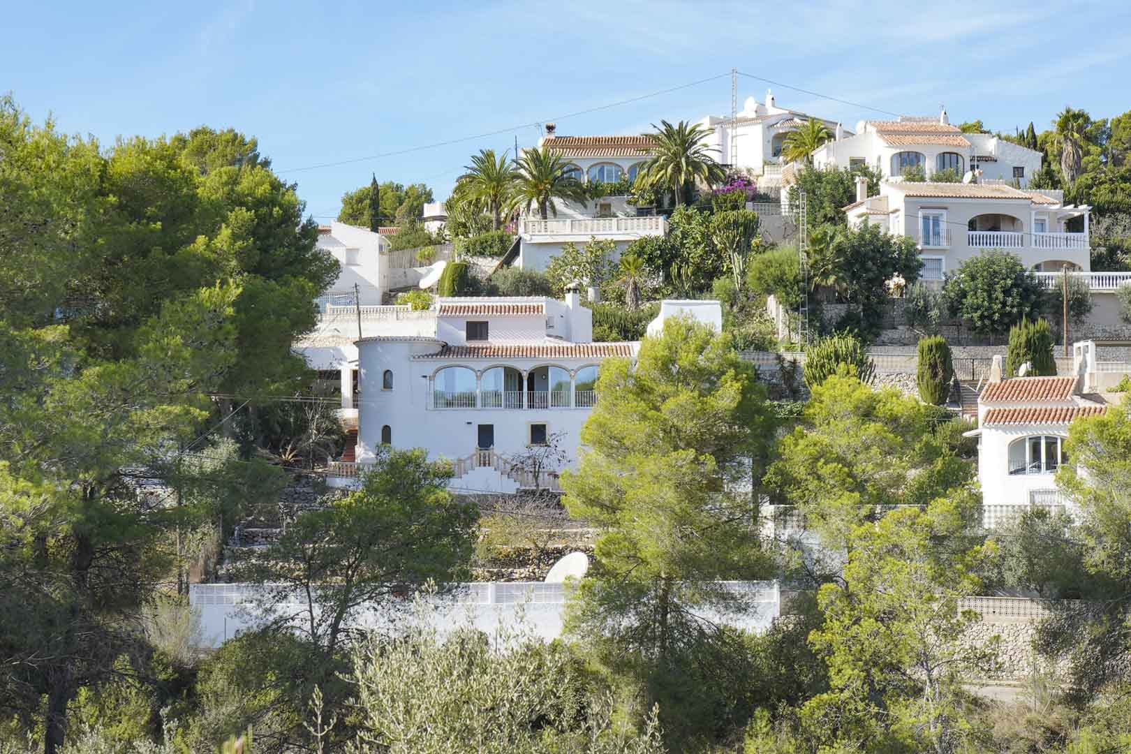 Außenansicht der mediterranen Villa in Hanglage, mit weißer Fassade, verglaster Naya mit Rundbögen und einem traditionellen Rundturm.