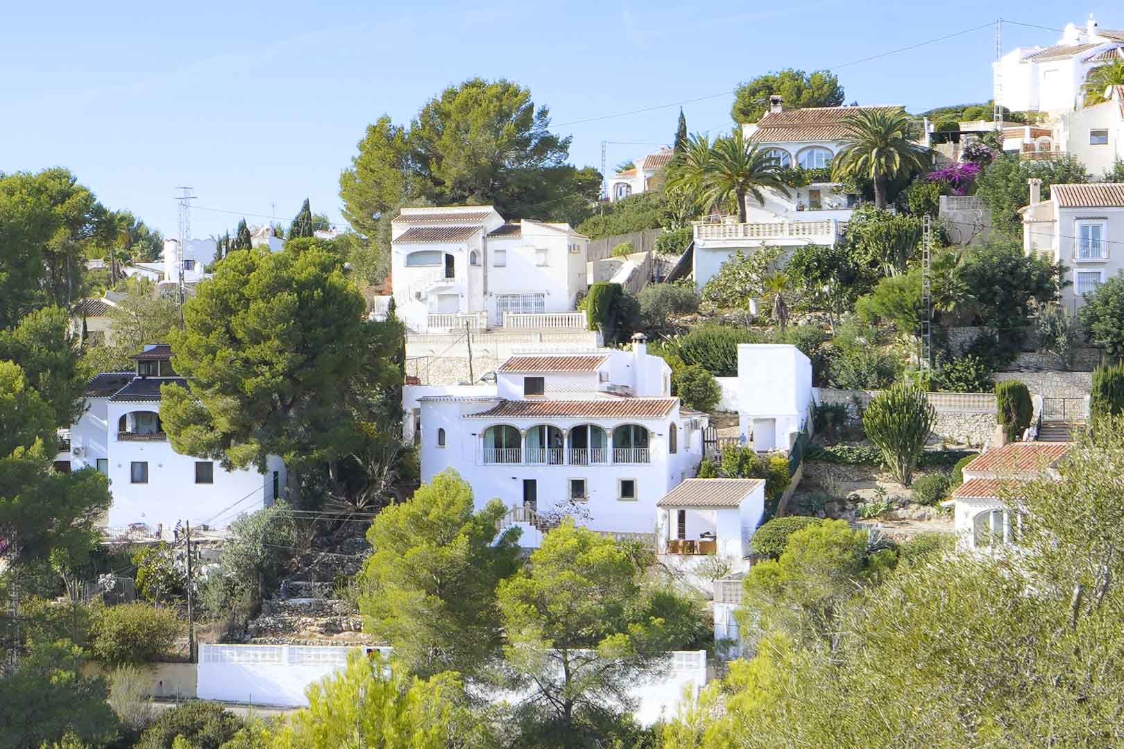Außenansicht der mehrstöckigen Villa mit traditioneller Rundbogen-Naya, weißen Fassaden und Terrakottadächern inmitten einer mediterranen Pinienlandschaft.
