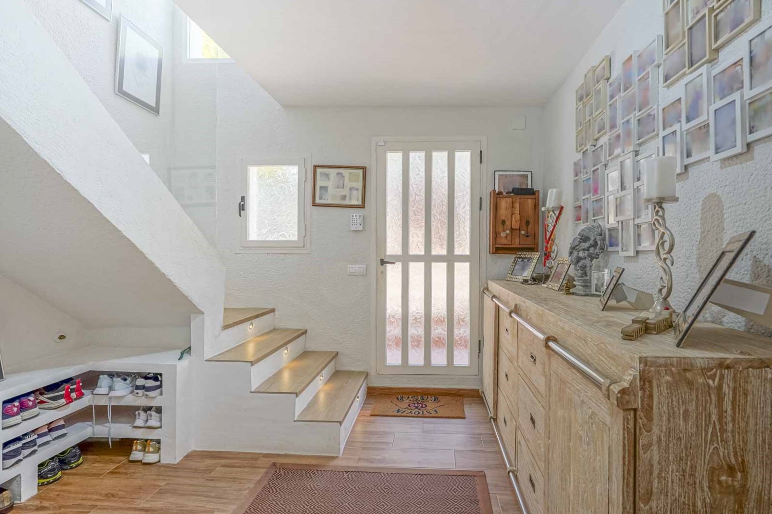 Heller Eingangsbereich mit Holztreppe und integrierter LED-Stufenbeleuchtung, rustikaler Anrichte und praktischem Stauraum unter der Treppe.