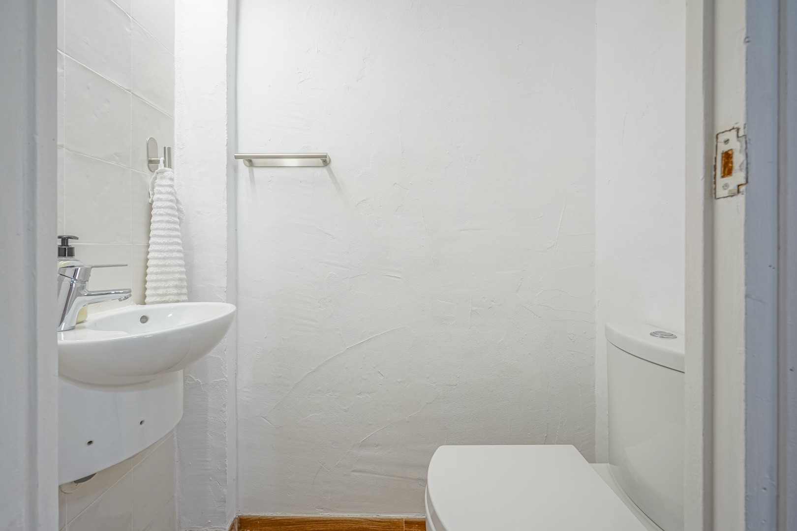 Kompaktes Gäste-WC mit strukturierten weißen Wänden, wandhängendem Keramikwaschbecken und verchromten Armaturen sowie einem Handtuchhalter aus Edelstahl.