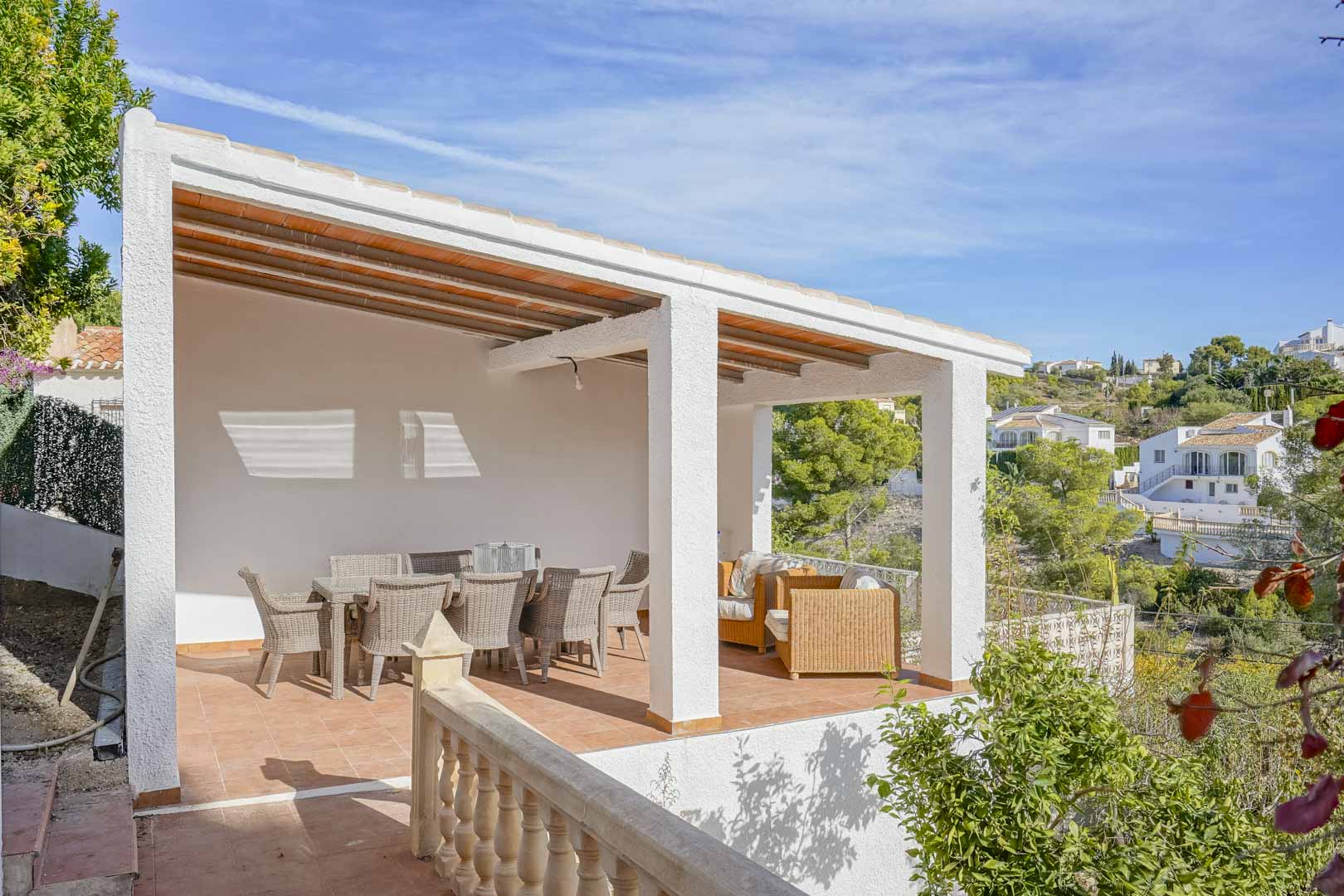 Überdachte Terrasse mit Holzbalkendecke, Korbmöbeln und weitem Blick über die umliegende Hügellandschaft von Jávea.