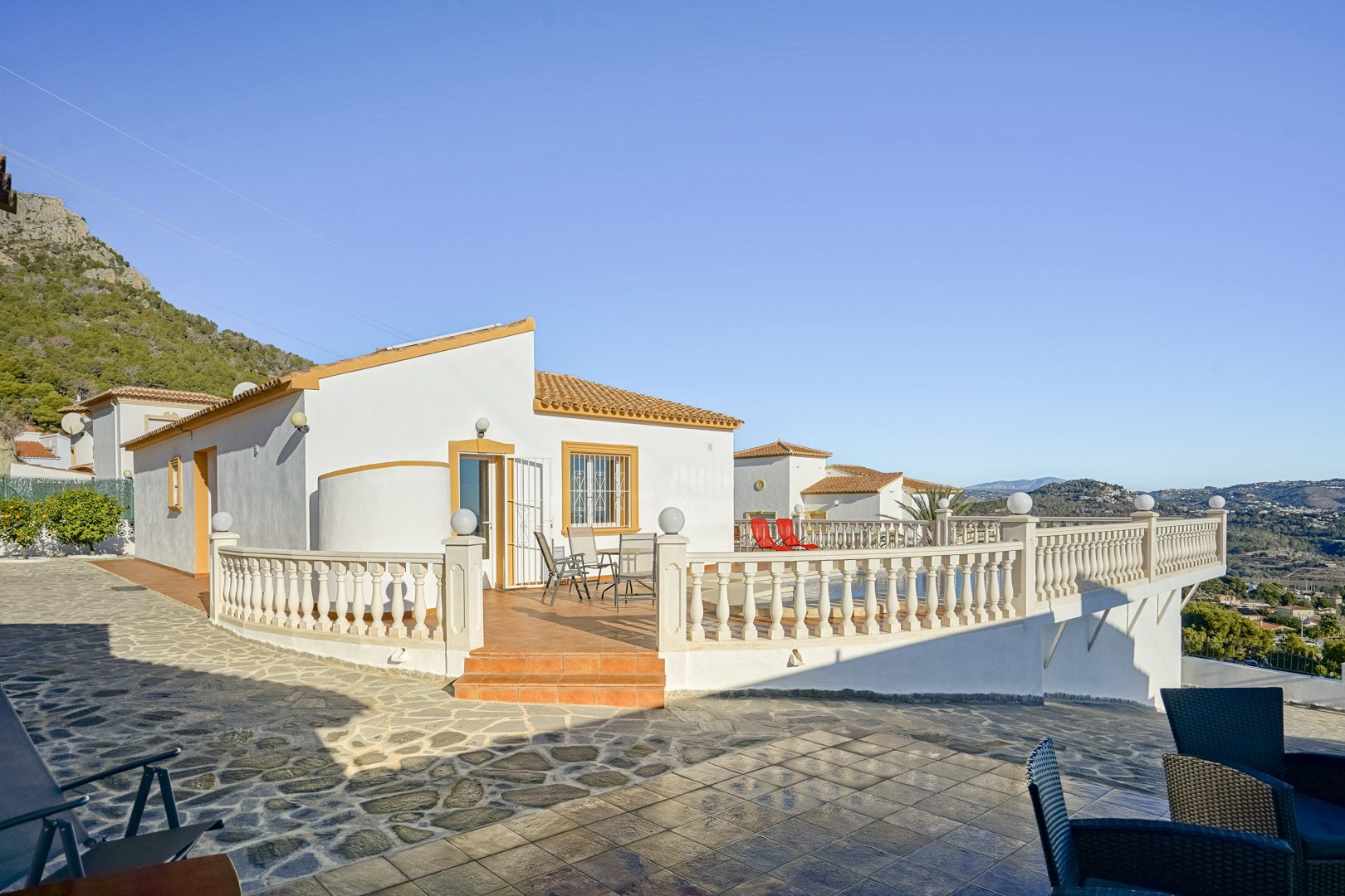 Außenansicht der Villa mit einer weitläufigen Terrakotta-Terrasse, klassischer Balustrade und Panoramablick auf die Küste und die Sierra de Oltà.