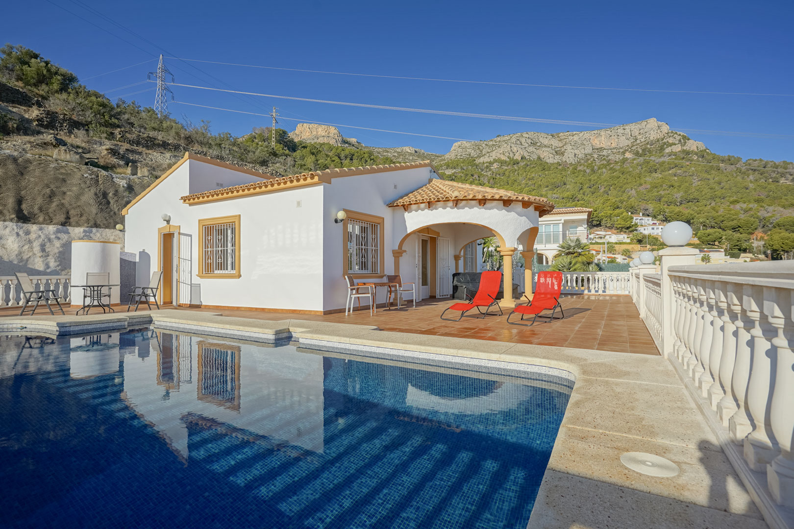 Außenansicht der Villa mit privatem Pool, weitläufiger Terrakotta-Terrasse und traditioneller Rundbogen-Naya vor der Kulisse der Sierra de Oltà.