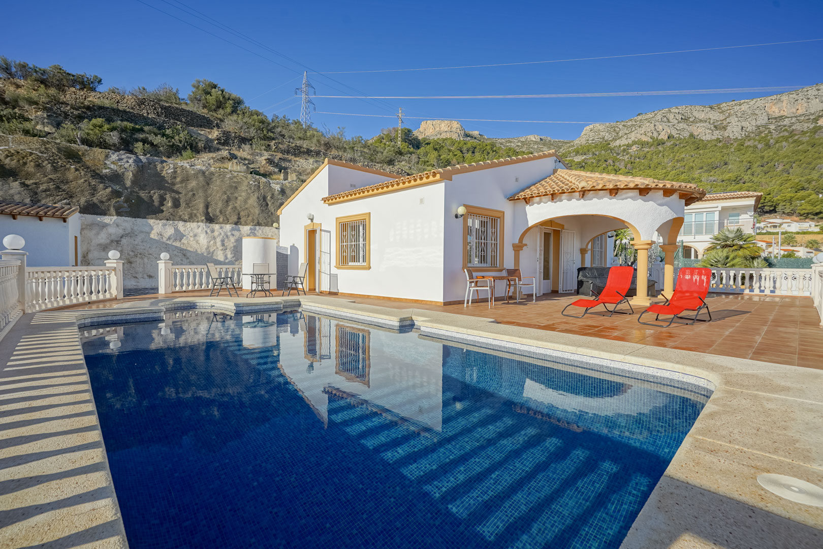 Außenansicht der Villa mit privatem Pool, weitläufiger Terrasse und bogenförmiger Veranda vor der Kulisse des Sierra de Oltà Gebirges.