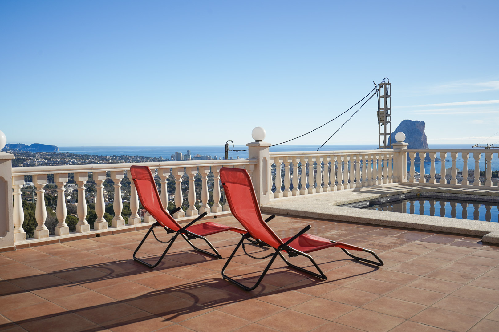 Erhöhte Terrasse mit Terrakottafliesen, weißer Balustrade und Panoramablick auf den Peñón de Ifach und das Mittelmeer am Poolbereich.