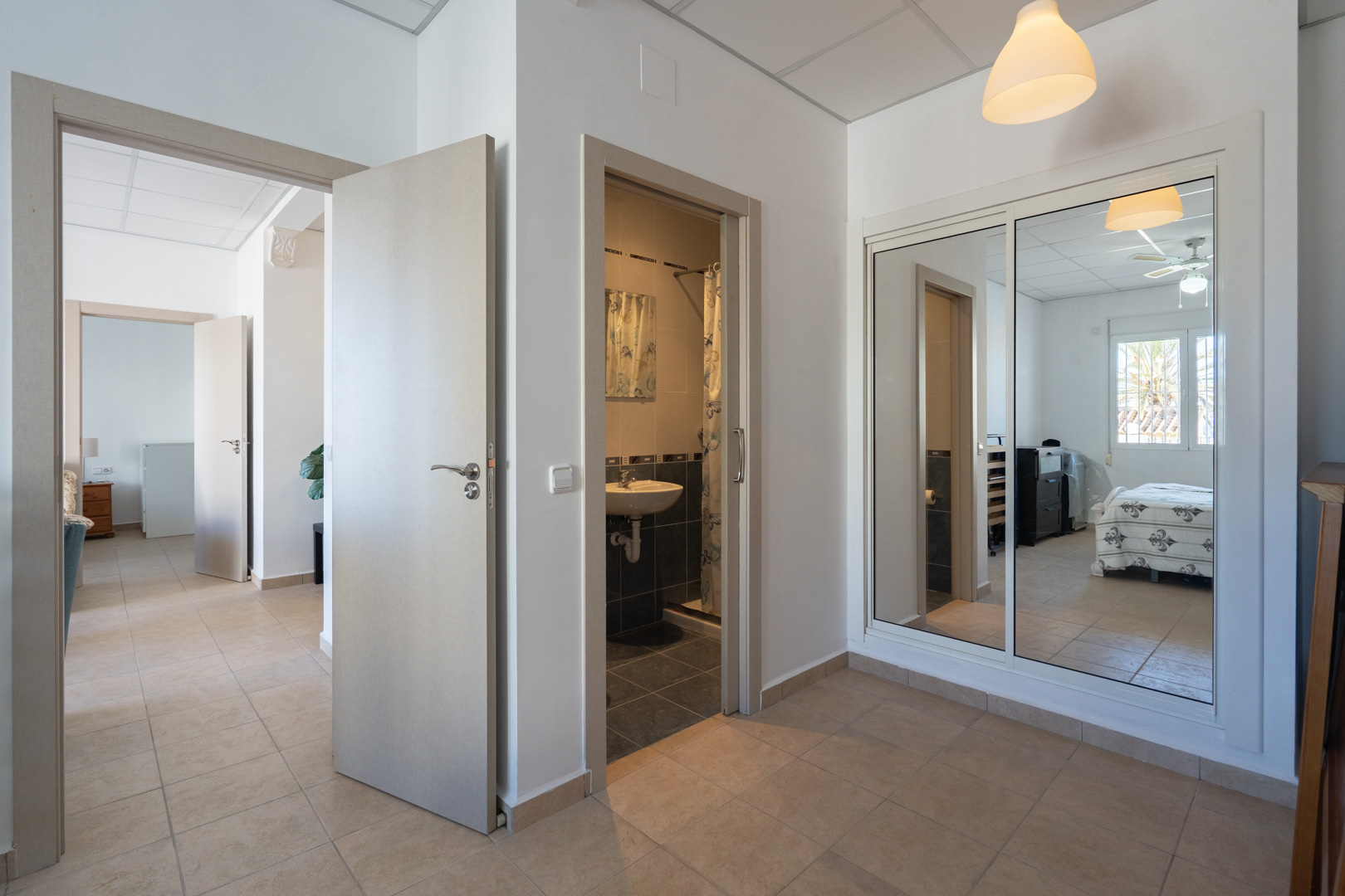 Flur mit Fliesenboden, Einbauschrank mit Spiegeltüren und Zugang zu einem Badezimmer sowie einem Schlafzimmer mit Deckenventilator.