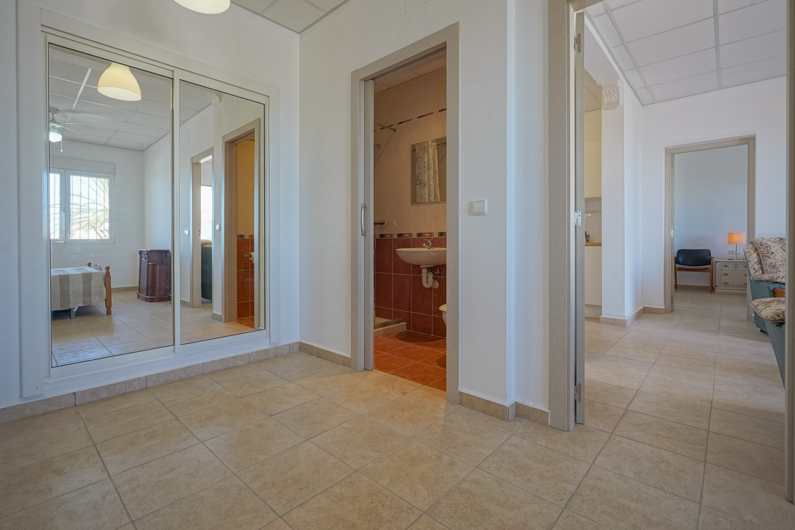 Flur mit Fliesenboden, großem Einbauschrank mit Spiegelschiebetüren und Zugang zu einem gefliesten Badezimmer sowie weiteren Wohnräumen.