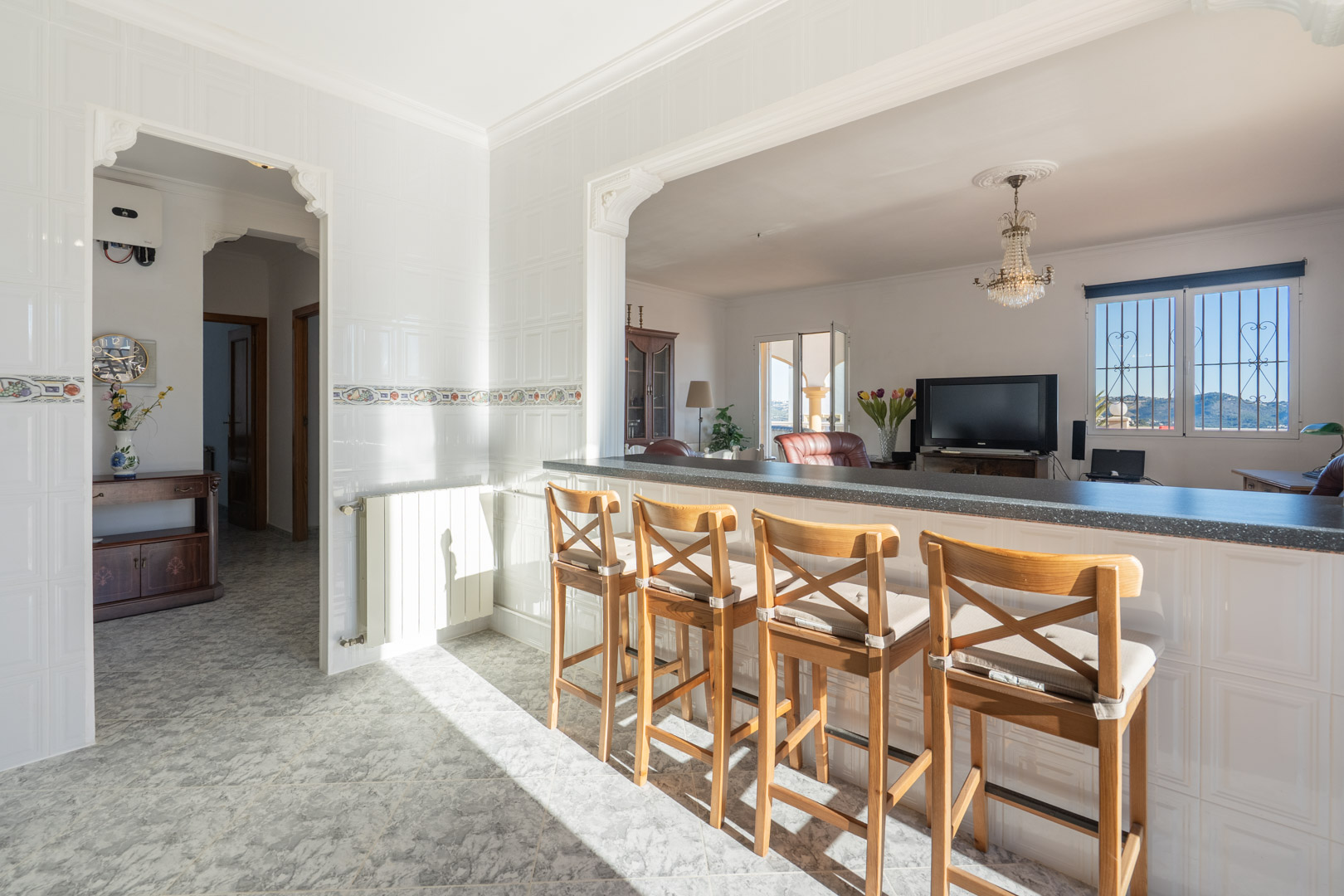 Küchenbar mit Holzstühlen und Blick auf das Wohnzimmer, mit weißen Fliesenwänden, traditionellen Rundbögen und Bergblick durch das Fenster.