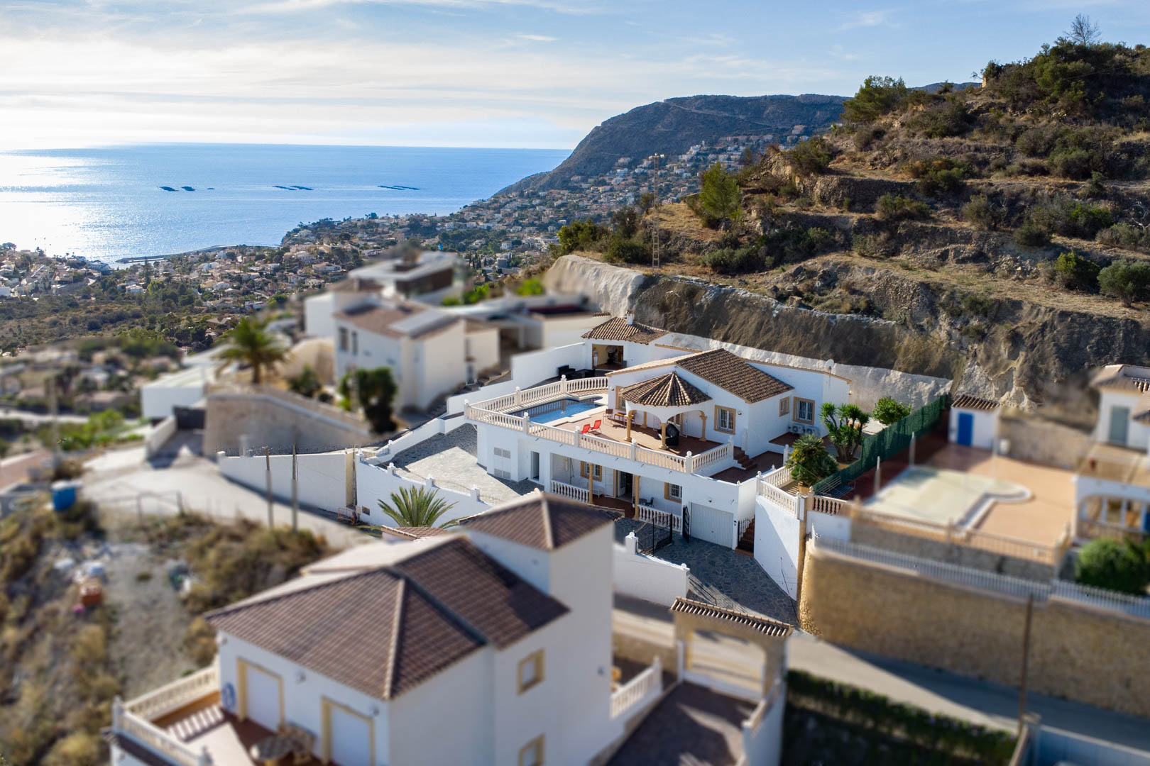 Luftaufnahme der Villa in Partida Cucarres mit Poolterrasse, traditionellem Ziegeldach und Panoramablick auf das Mittelmeer und die Küstenlinie.