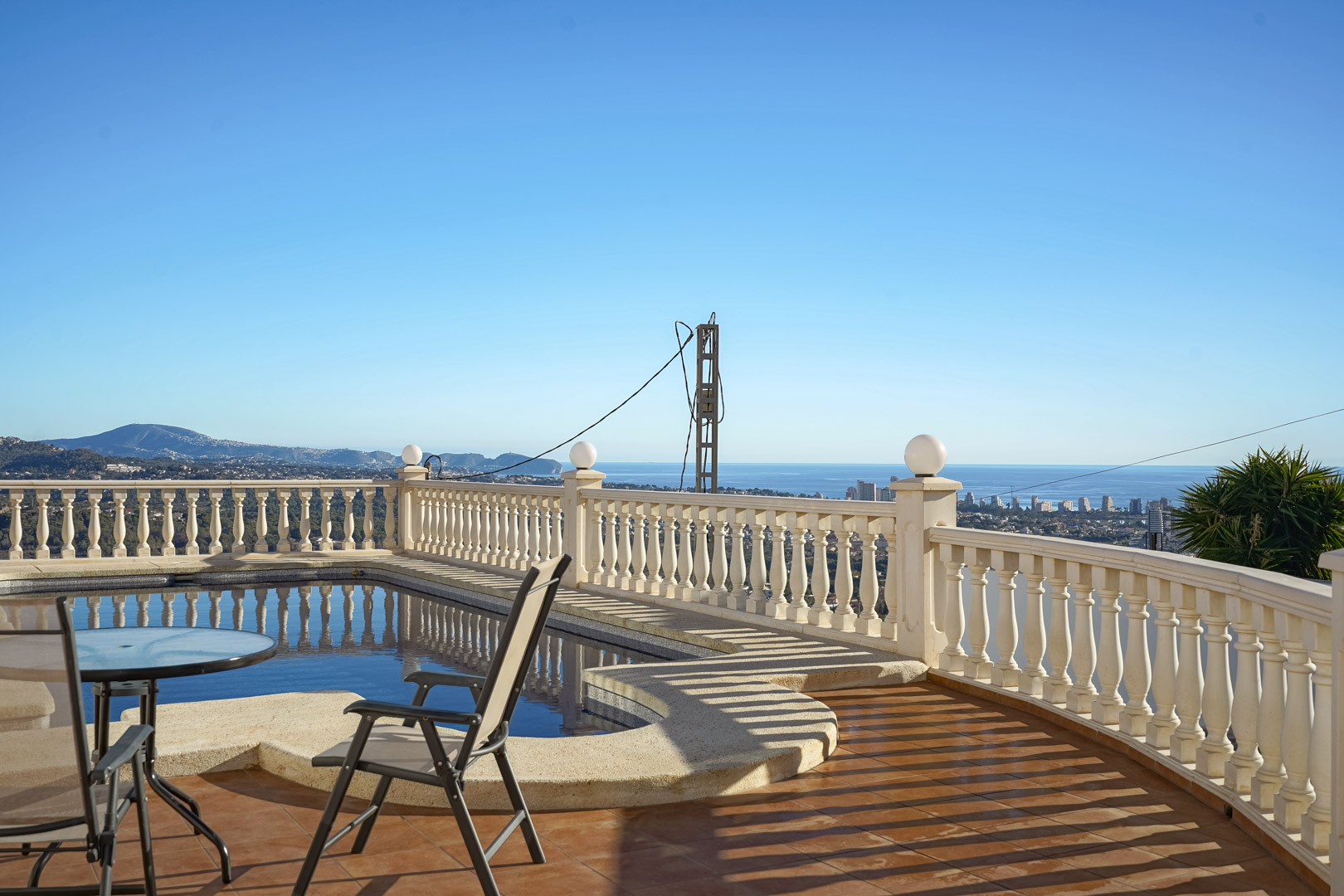 Poolterrasse mit klassischer Balustrade und Terrakottaboden, die einen weiten Blick auf das Mittelmeer und die Skyline von Calpe bietet.
