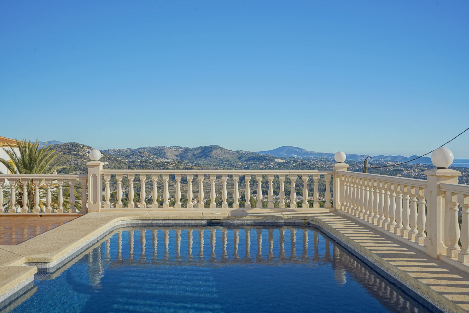 Rechteckiger Swimmingpool mit klassischer Steinbalustrade und Panoramablick auf die Mittelmeerküste und die umliegende Berglandschaft der Marina Alta.