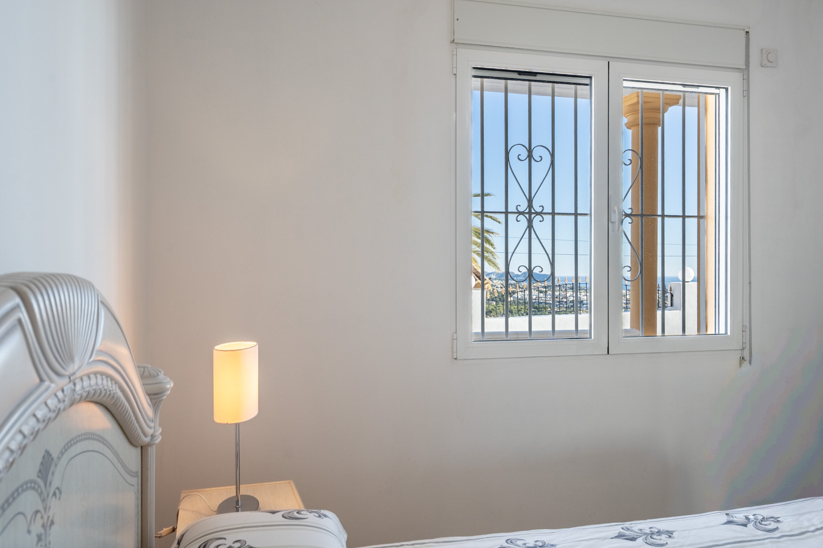 Schlafzimmer mit klassisch geschnitztem Kopfteil und Fenster mit Ziermetallgitter, das Ausblicke auf die Küste von Calpe und das Meer bietet.