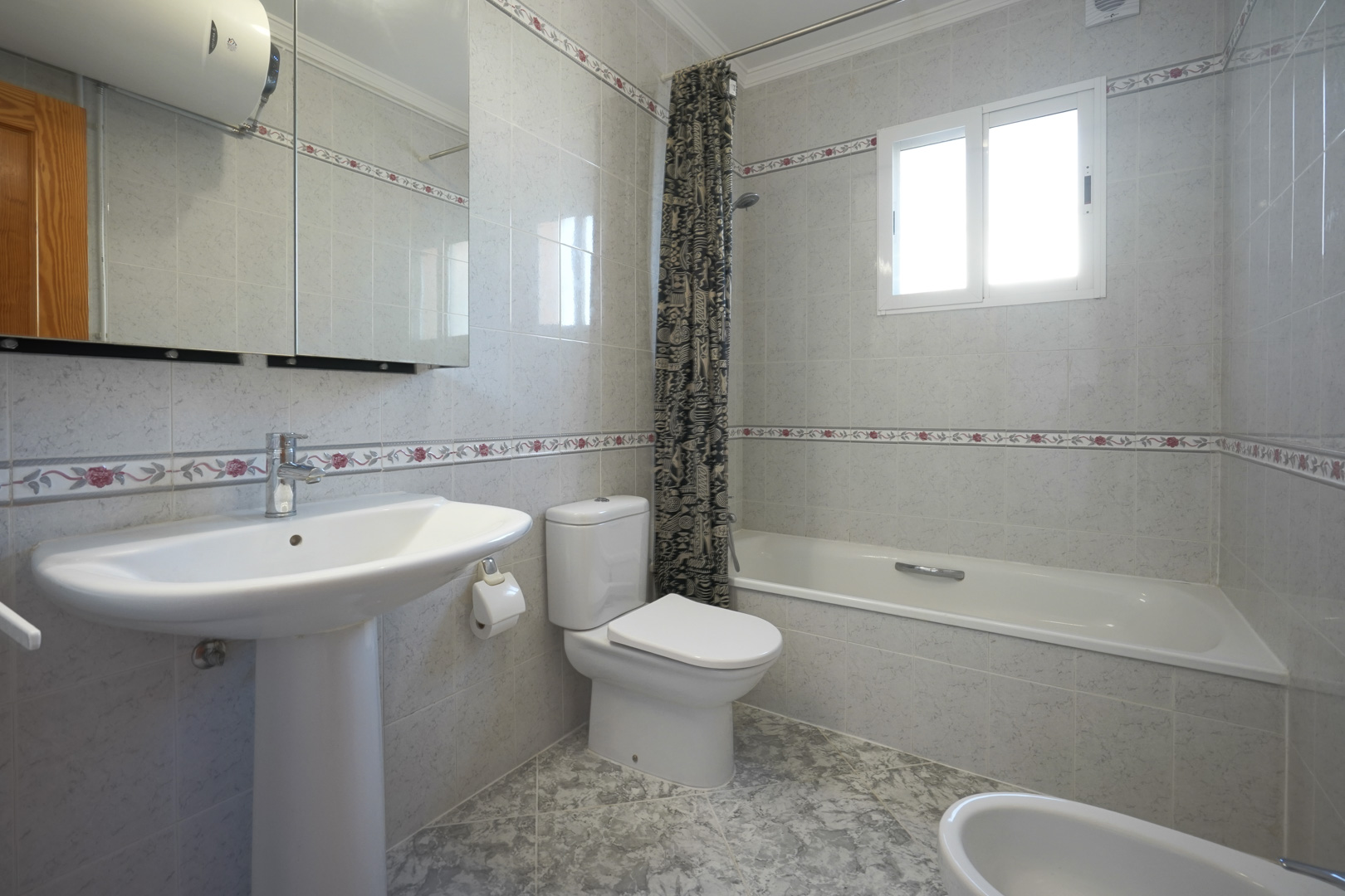 Traditionelles Badezimmer mit floralen Bordürenfliesen, ausgestattet mit Badewanne, Säulenwaschbecken, Bidet und einem Spiegelschrank.