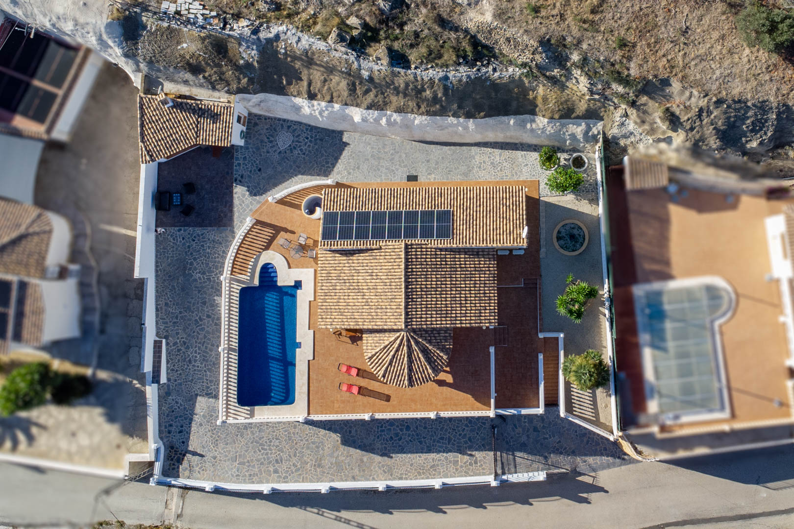 Vogelperspektive der Villa mit Ziegeldach, Photovoltaikmodulen, privatem Pool und weitläufigen Terrassenflächen aus Stein und Keramik.