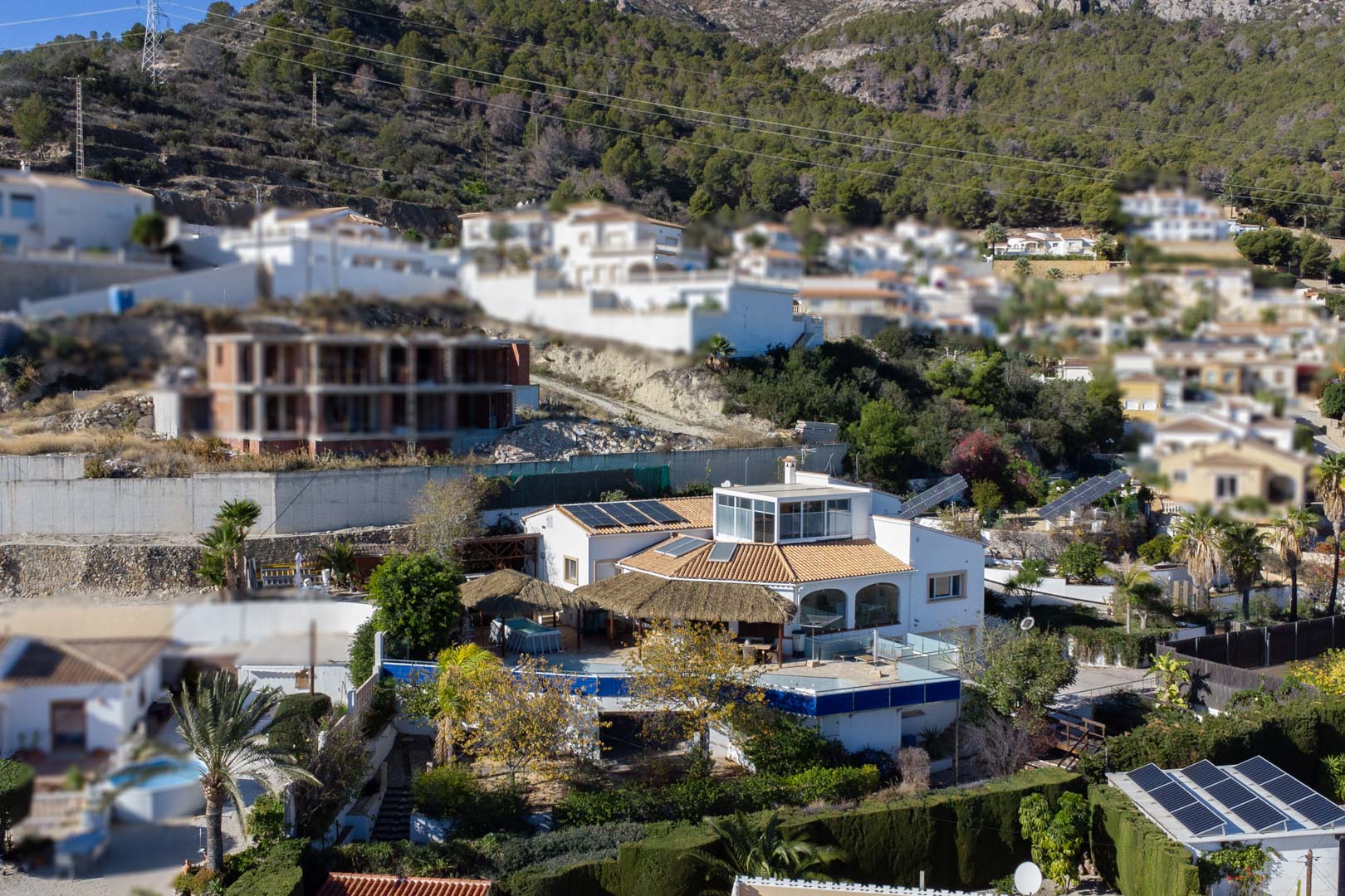 Außenansicht der mehrstöckigen Villa mit Photovoltaikanlagen, verglaster Dachterrasse und weitläufigen Außenbereichen mit Reetdach-Pergolen in Hanglage von Calpe.