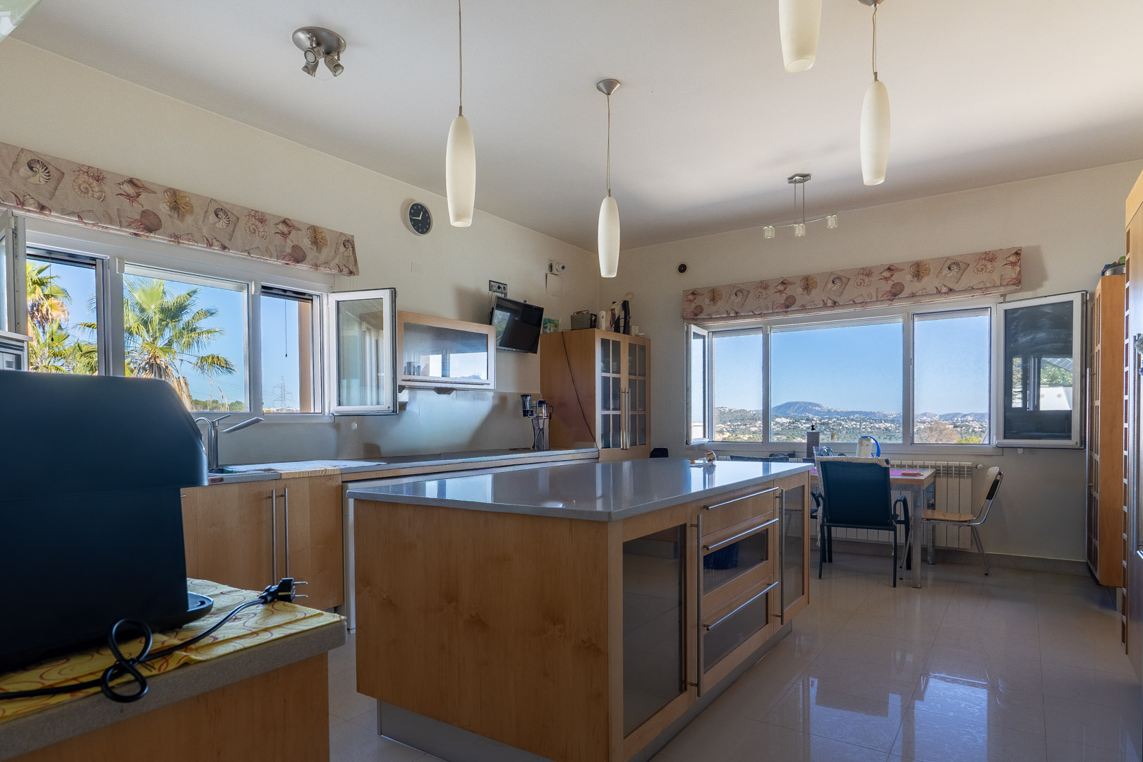 Großzügige Küche mit zentraler Kochinsel aus Holz und grauen Arbeitsplatten. Große Fensterfronten bieten einen weiten Blick auf das Meer und die Küstenlandschaft.