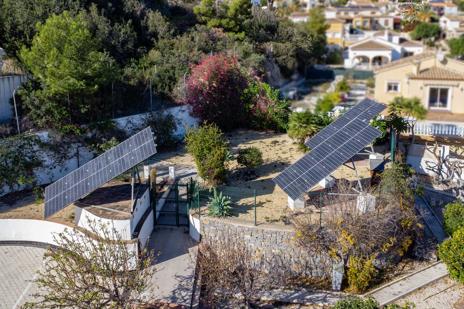 Luftaufnahme der Photovoltaikanlage mit drei motorisierten Solartürmen auf dem Grundstück, umgeben von mediterraner Bepflanzung und Natursteinmauern.