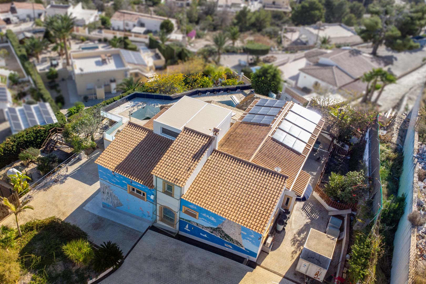 Luftaufnahme der Villa mit traditionellem Ziegeldach, installierten Solarmodulen und einem großflächigen Wandgemälde des Peñón de Ifach an der Fassade.