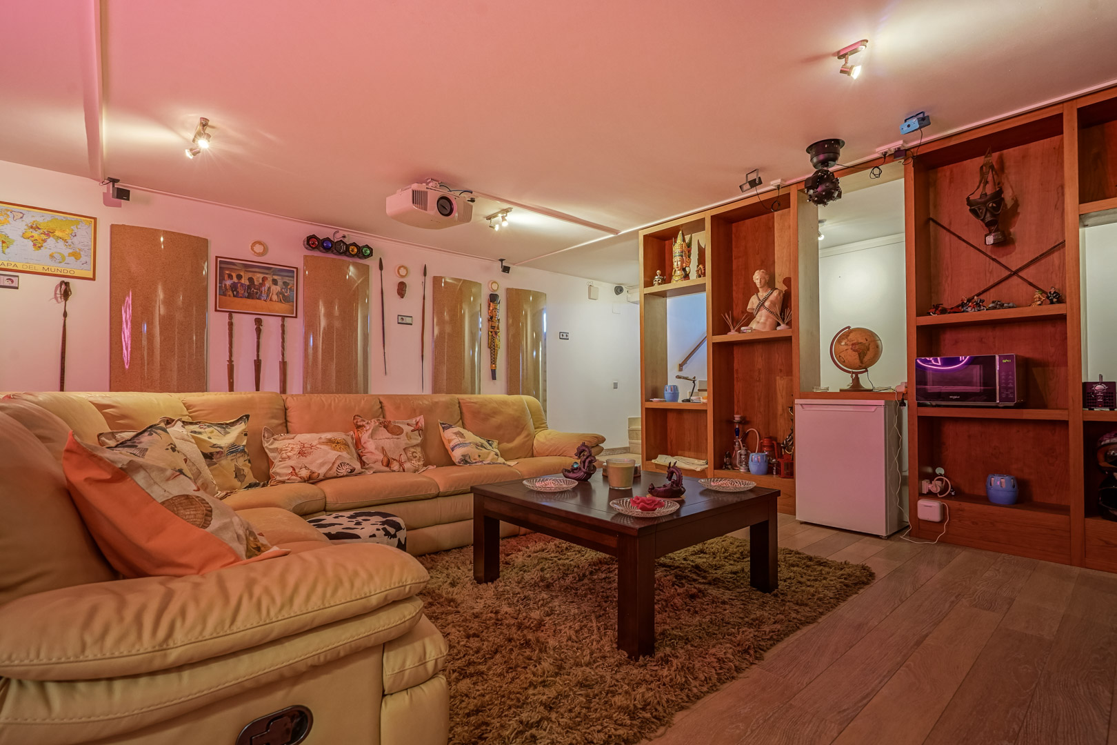 Multimediaraum mit Leder-Ecksofa, Deckenprojektor, Discolichtern und integriertem Holzregal inklusive Minikühlschrank und Mikrowelle.