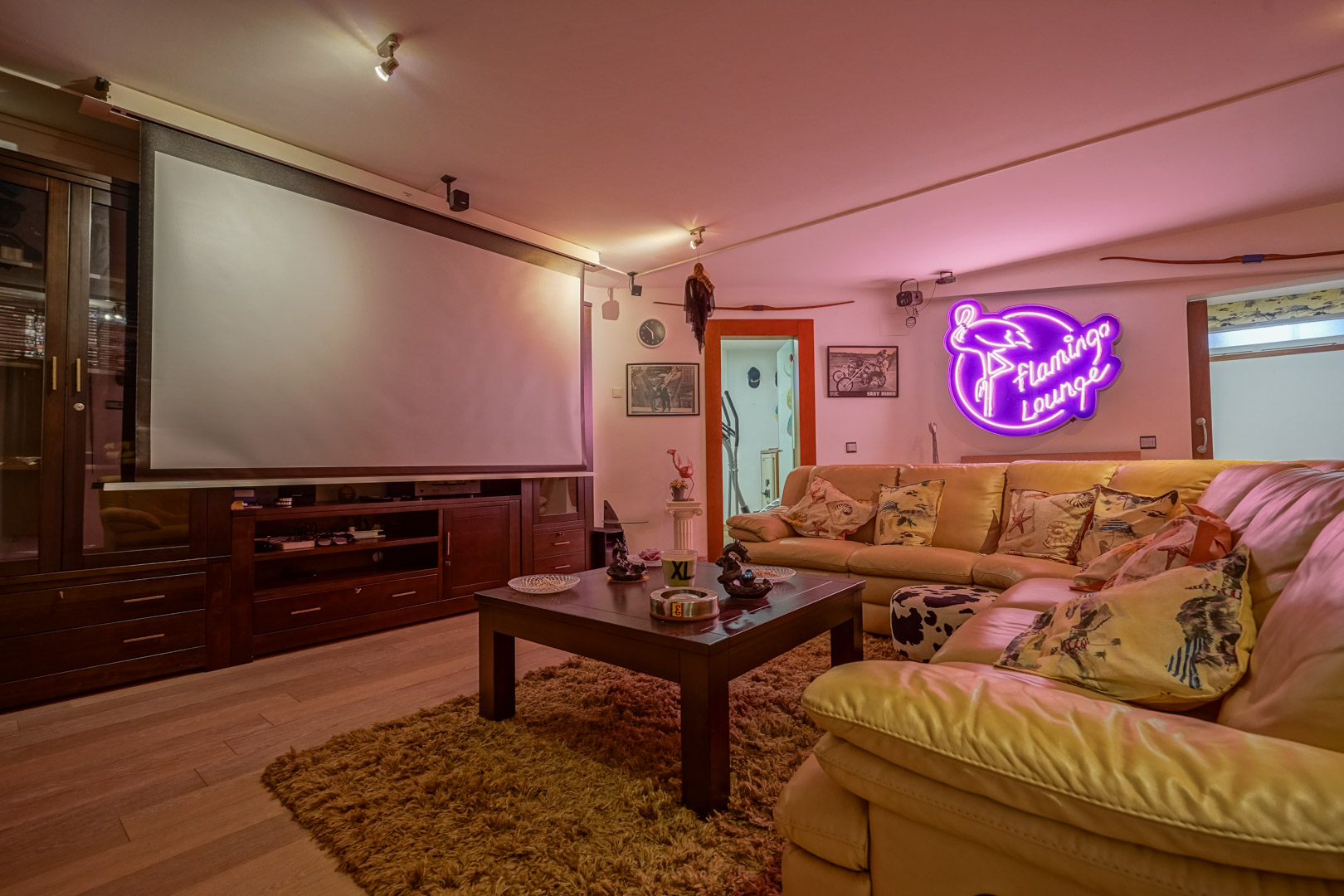Multimediaraum mit Projektionsleinwand, maßgefertigten dunklen Holzmöbeln und Lederecksofa. Neon-Ambientebeleuchtung und Parkettboden ergänzen die Ausstattung.