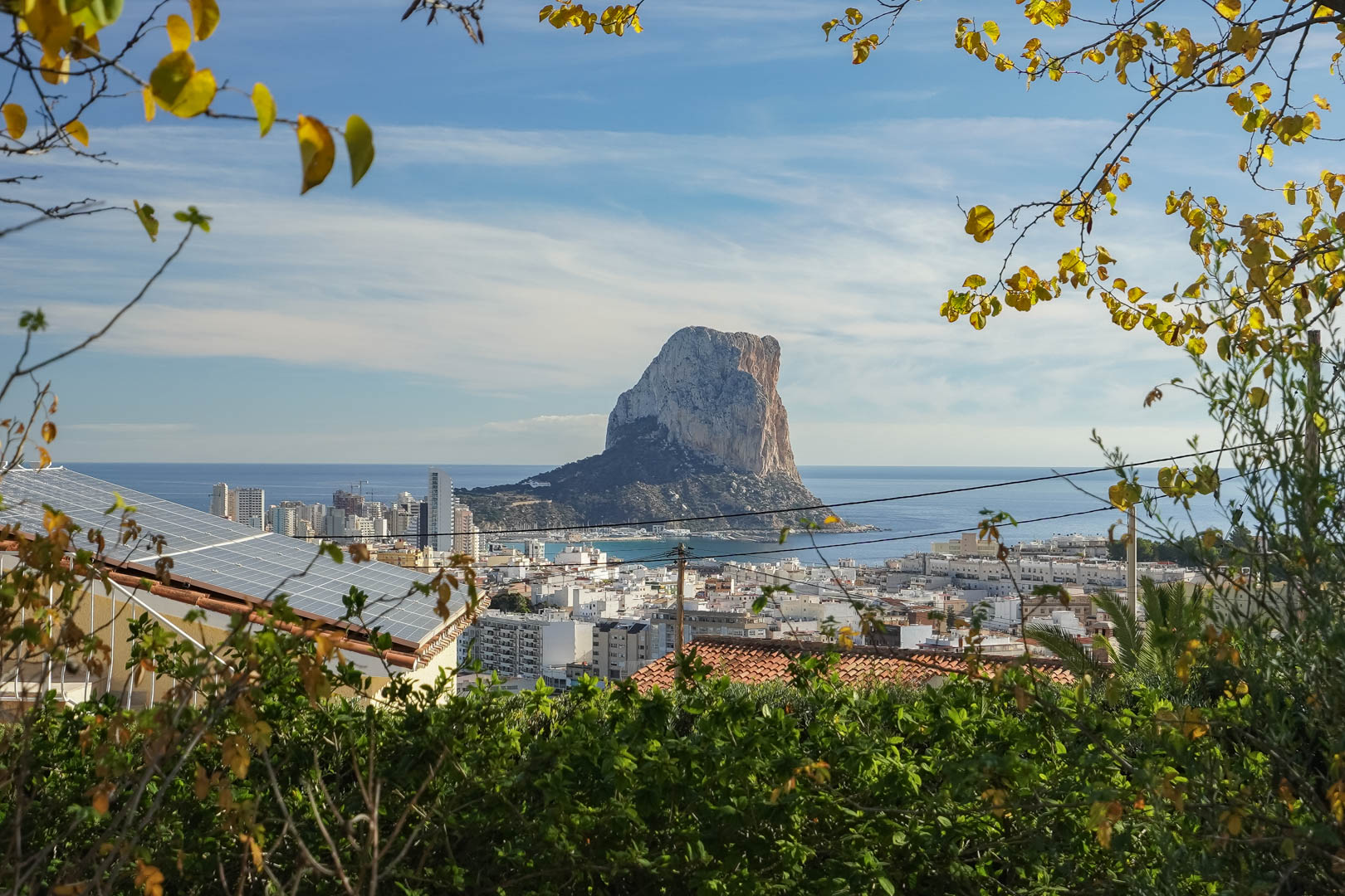 Panoramablick auf den Peñón de Ifach und die Skyline von Calpe, mit Sicht auf die Solaranlage auf dem Dach, umrahmt von mediterraner Vegetation.