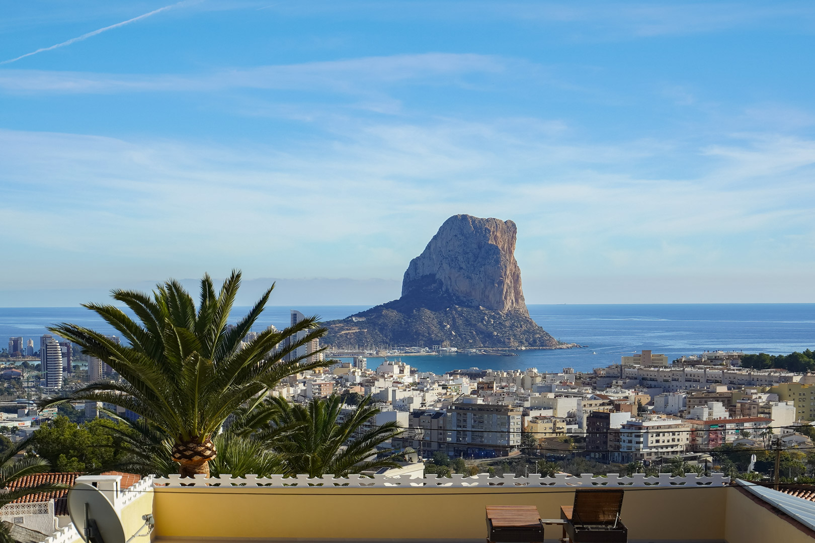 Panoramablick von der Terrasse auf den Peñón de Ifach und die Skyline von Calpe, mit dem Mittelmeer im Hintergrund und Sonnenliegen im Vordergrund.