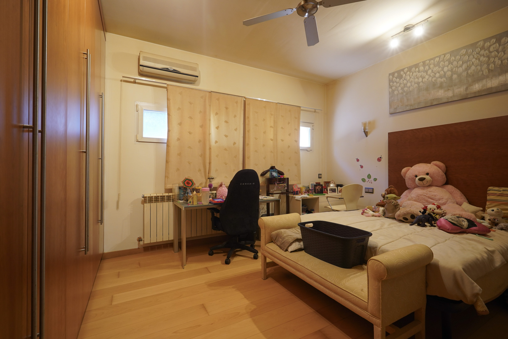 Schlafzimmer mit edlen Holzböden, großen Einbauschränken aus Holz, Schreibtischbereich, Klimaanlage und Deckenventilator.