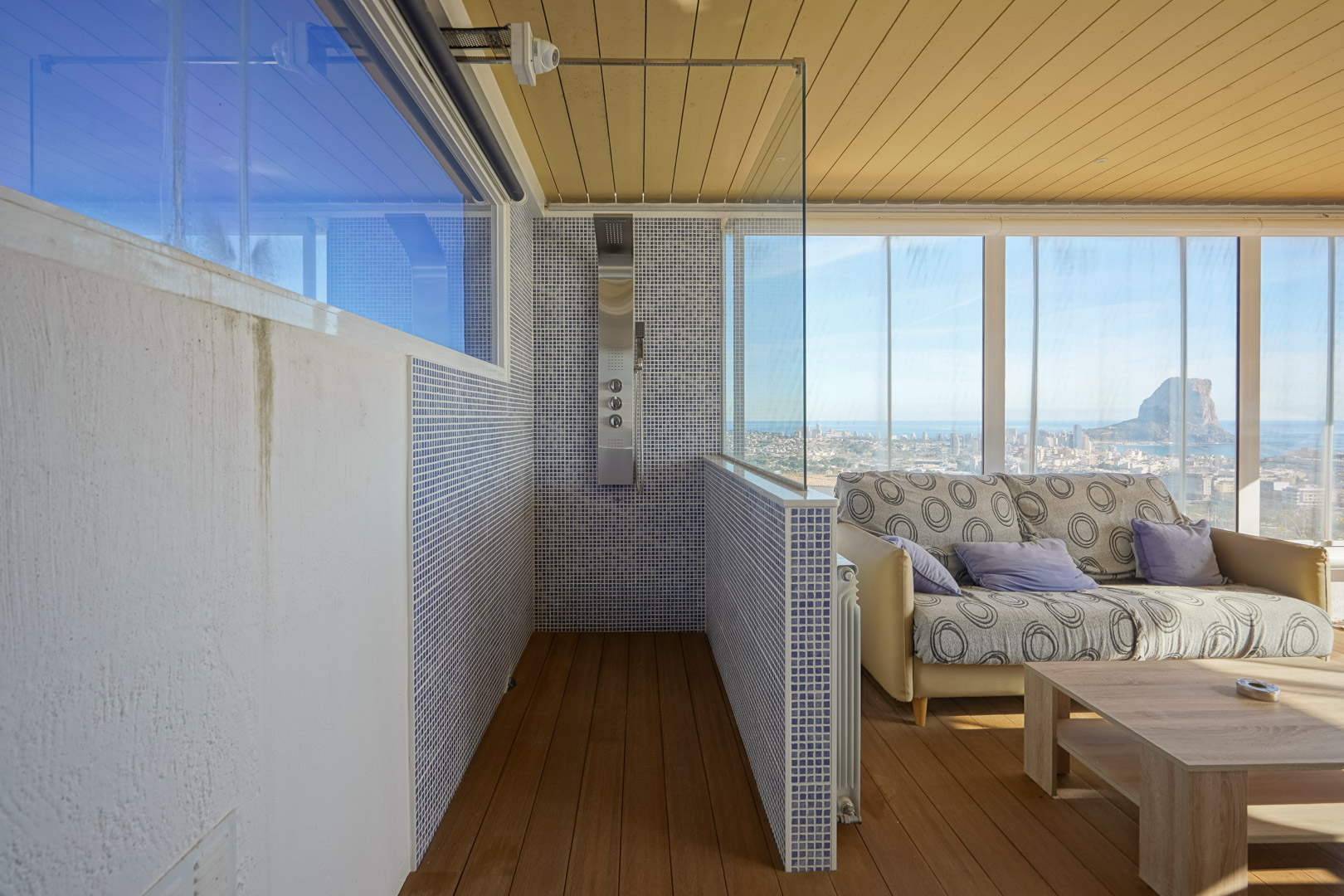 Wellnessbereich im Obergeschoss mit Hydromassage-Dusche, blauen Mosaikfliesen und verglastem Wohnbereich mit Panoramablick auf den Peñón de Ifach.