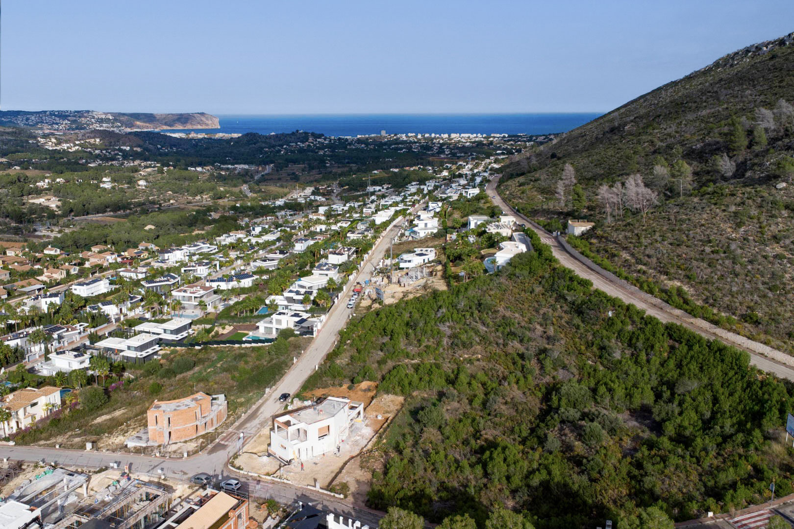 Luftaufnahme des Baugrundstücks in Monte Olímpico, Jávea, mit Blick auf moderne Villen und das Mittelmeer bis hin zum Kap San Antonio.
