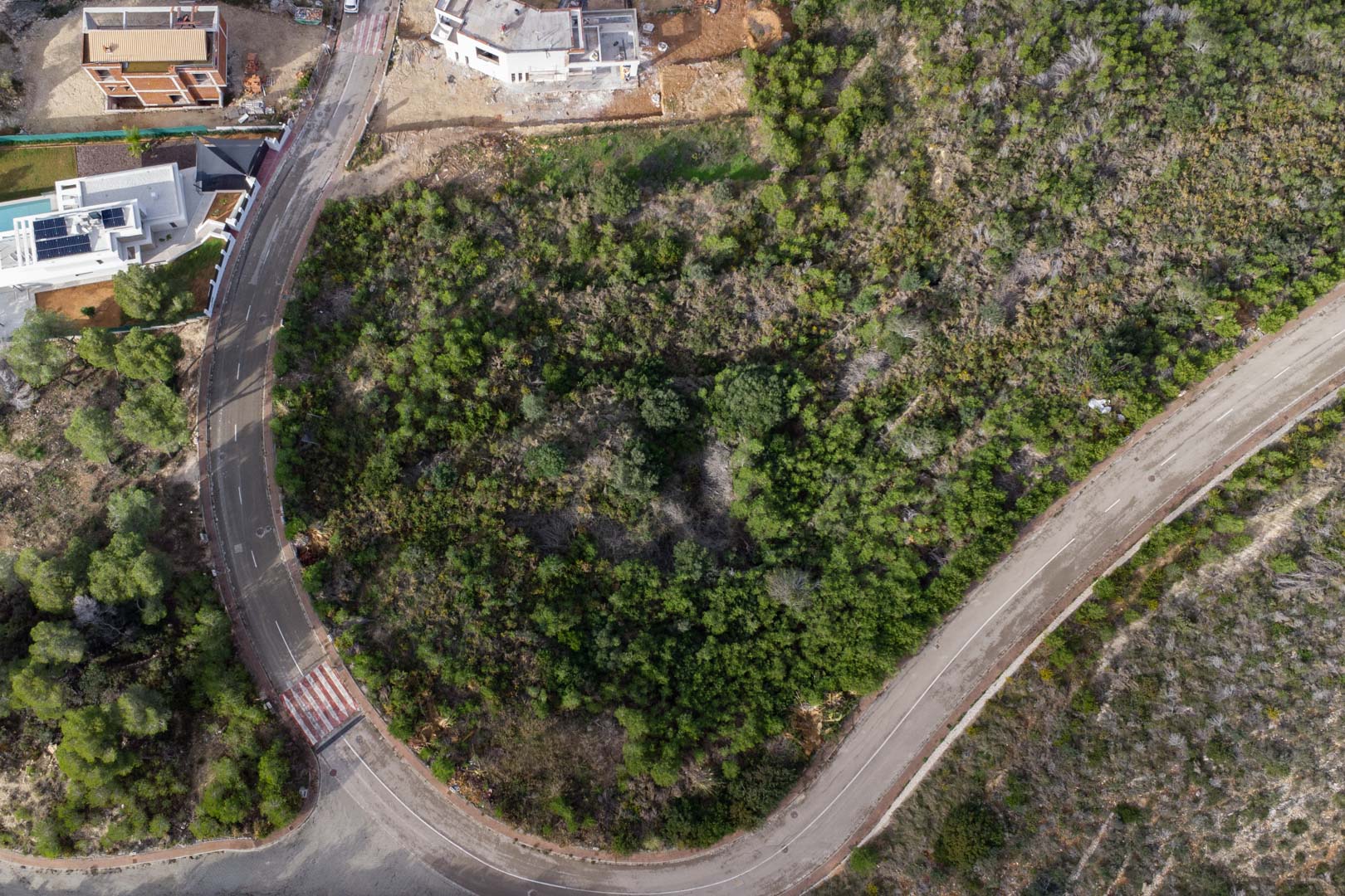 Luftaufnahme des Eckgrundstücks in Monte Olímpico, erschlossen durch asphaltierte Straßen mit Gehwegen und bewachsen mit typisch mediterraner Flora.